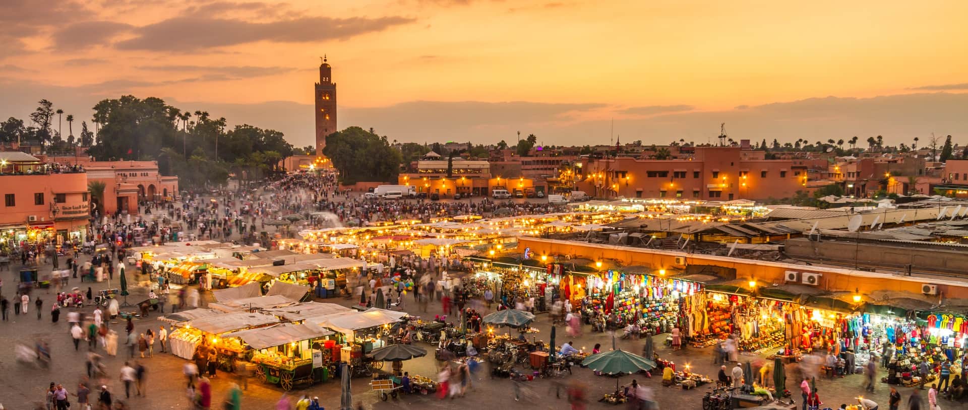 Plaza Jemaa el-Fna de Marrakech al atardecer con puestos de comida iluminados y minarete de la Koutoubia al fondo