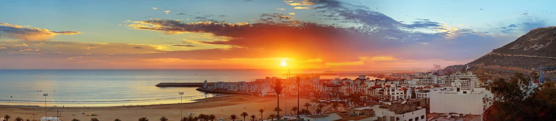 Panorámica de la bahía de Agadir al atardecer con cielo naranja, playa dorada y ciudad frente al Atlántico