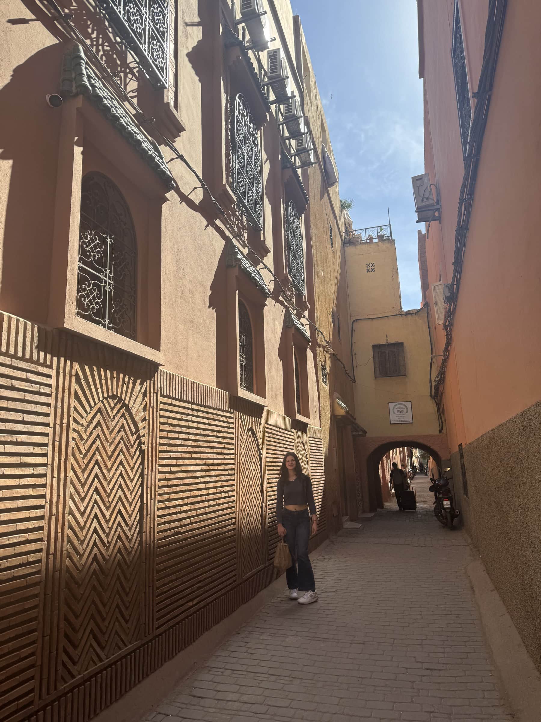 Callejón de la medina de Marrakech con puerta decorada en ladrillo y arco al fondo, ciudad roja de Marruecos