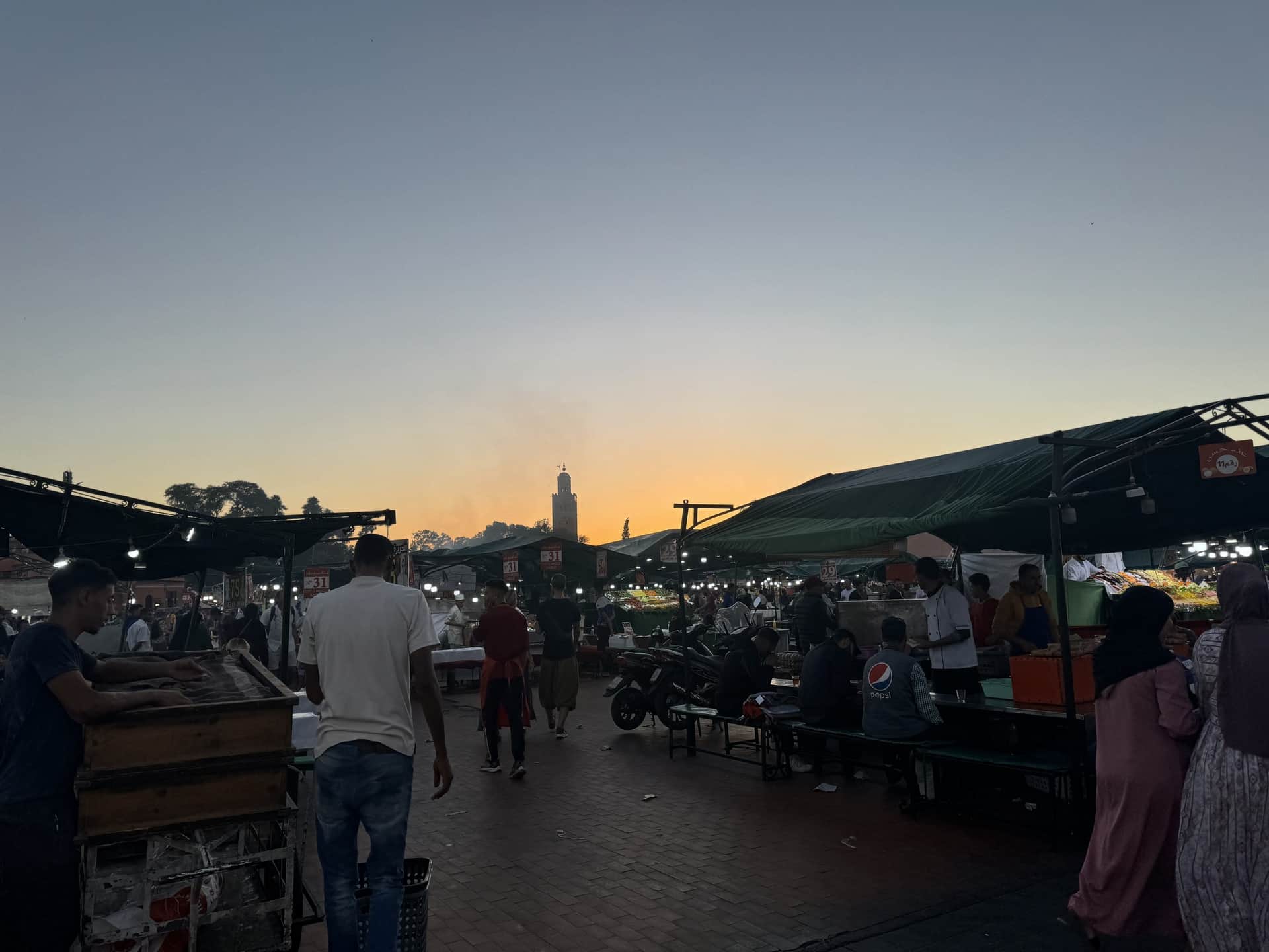 Atardecer en la plaza Jemaa el-Fna de Marrakech con puestos de comida y minarete de la Koutoubia al fondo