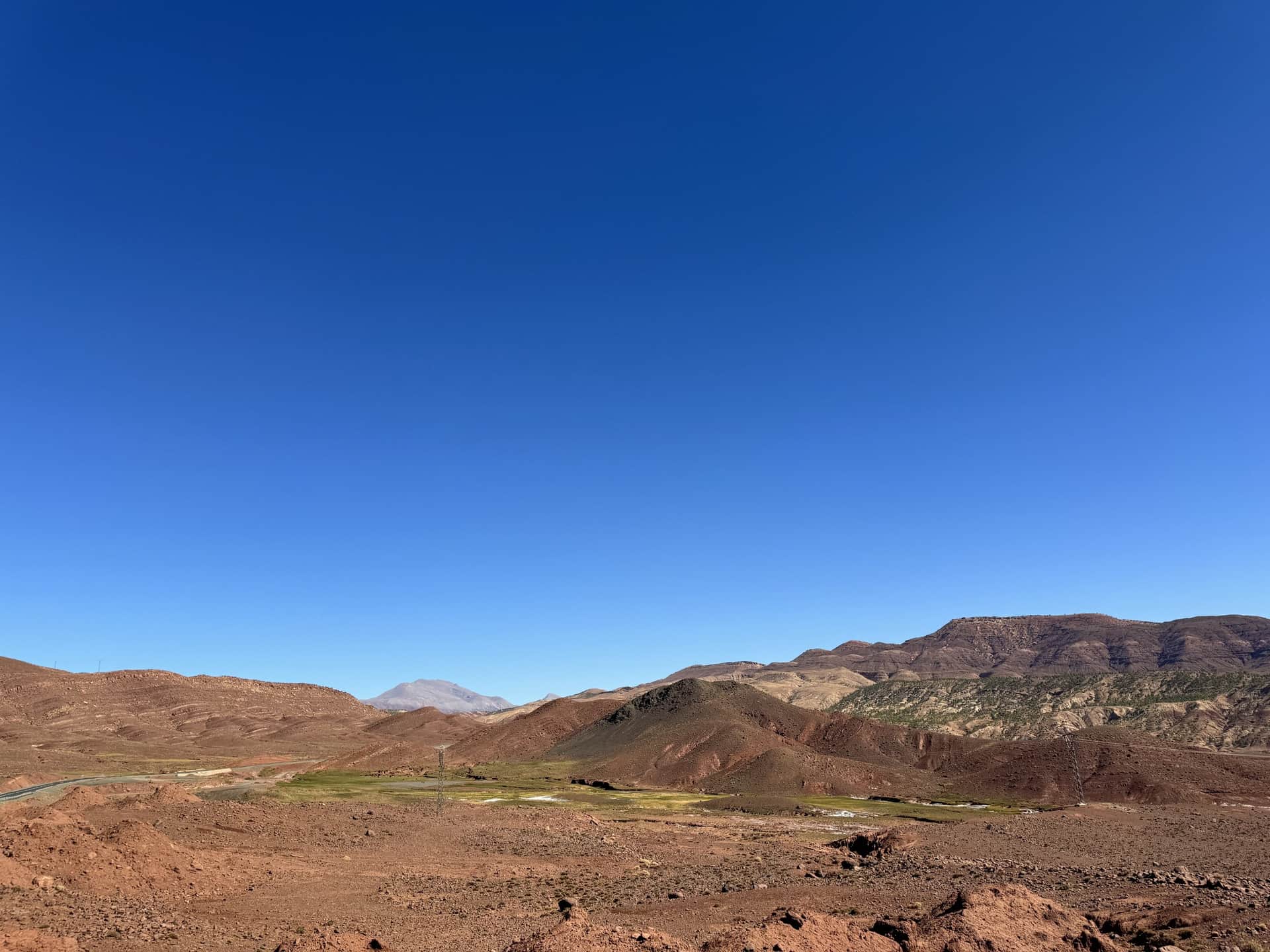 Valle árido del Alto Atlas marroquí con tierras rojizas, vegetación en el fondo y cielo azul intenso