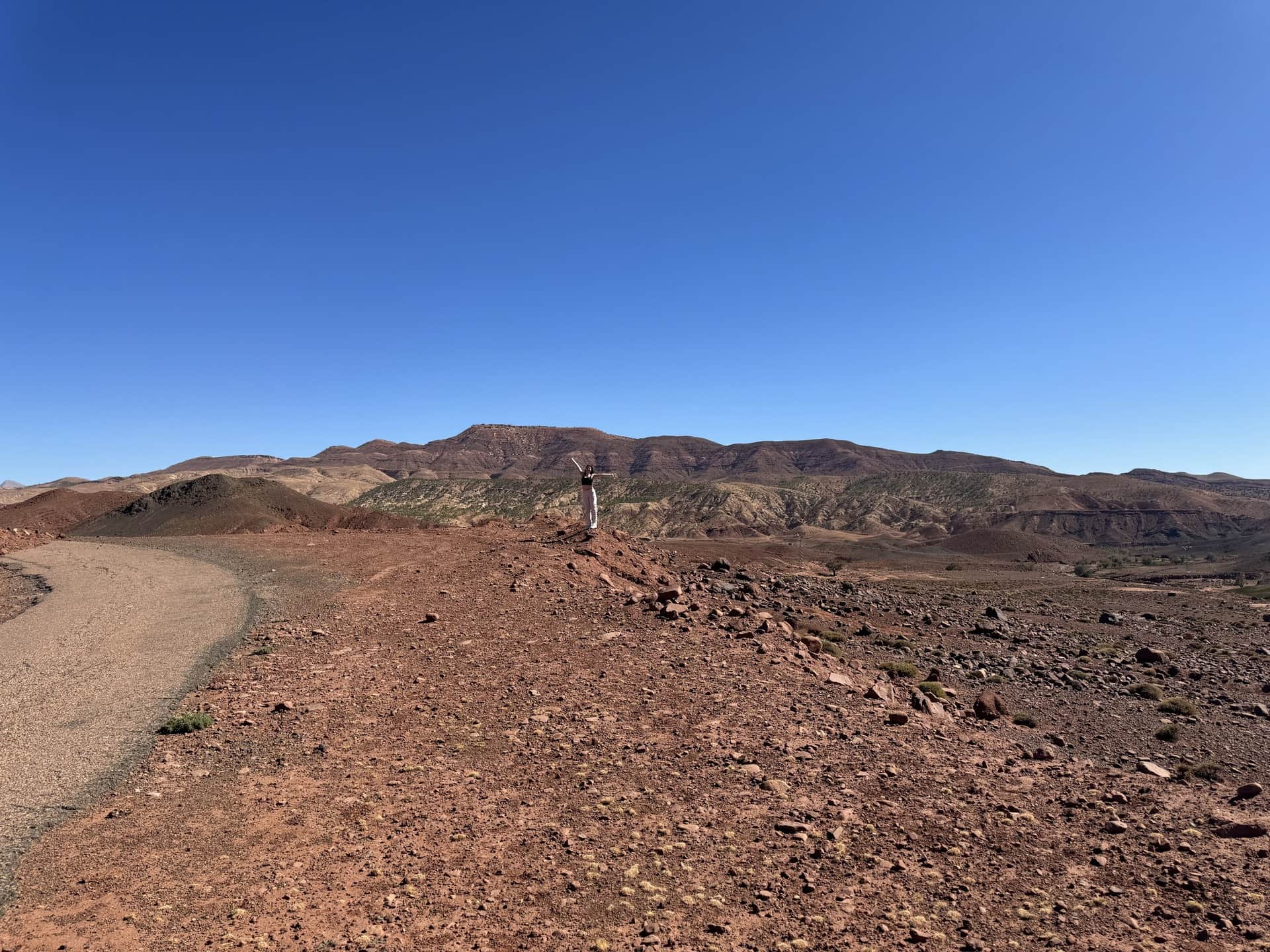 Viajera con los brazos abiertos en paisaje desértico rocoso del sur de Marruecos bajo cielo azul intenso