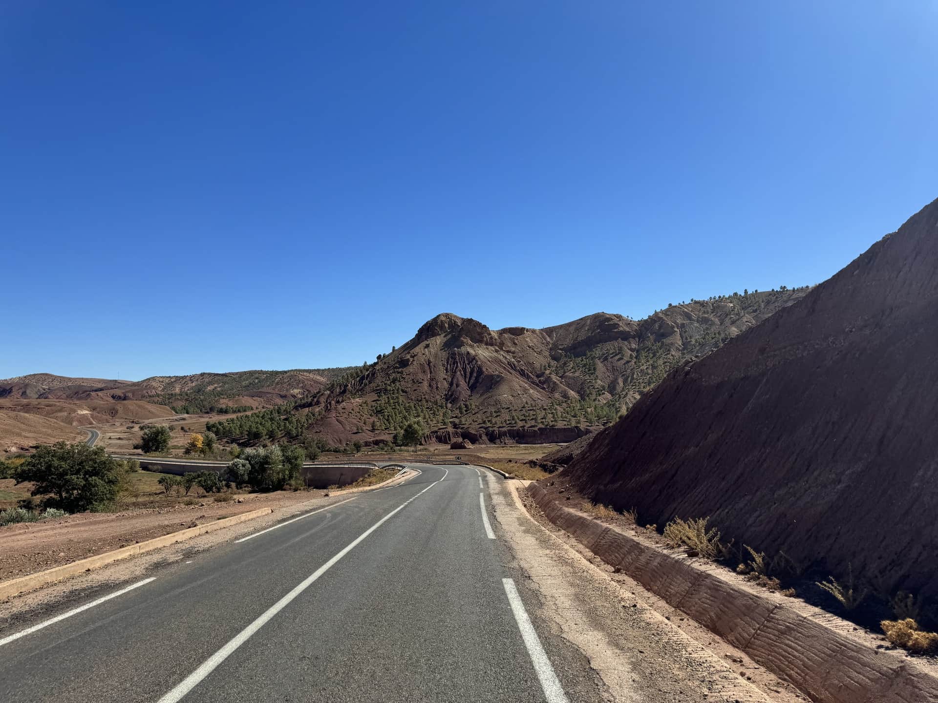 Carretera sinuosa entre montañas rojizas del Alto Atlas marroquí bajo un cielo azul intenso