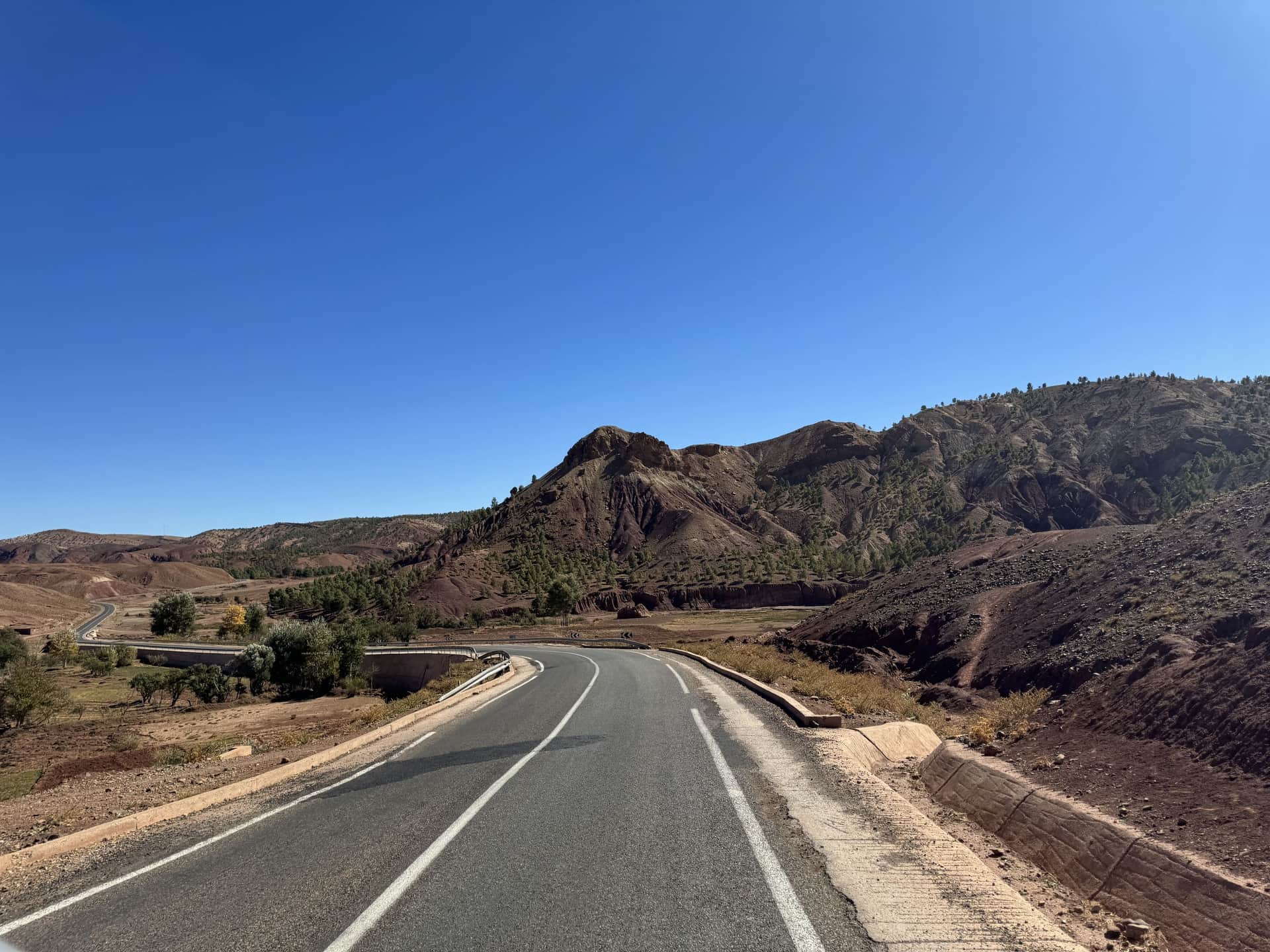 Carretera sinuosa atravesando el Alto Atlas marroquí con montañas rojizas y cielo azul despejado