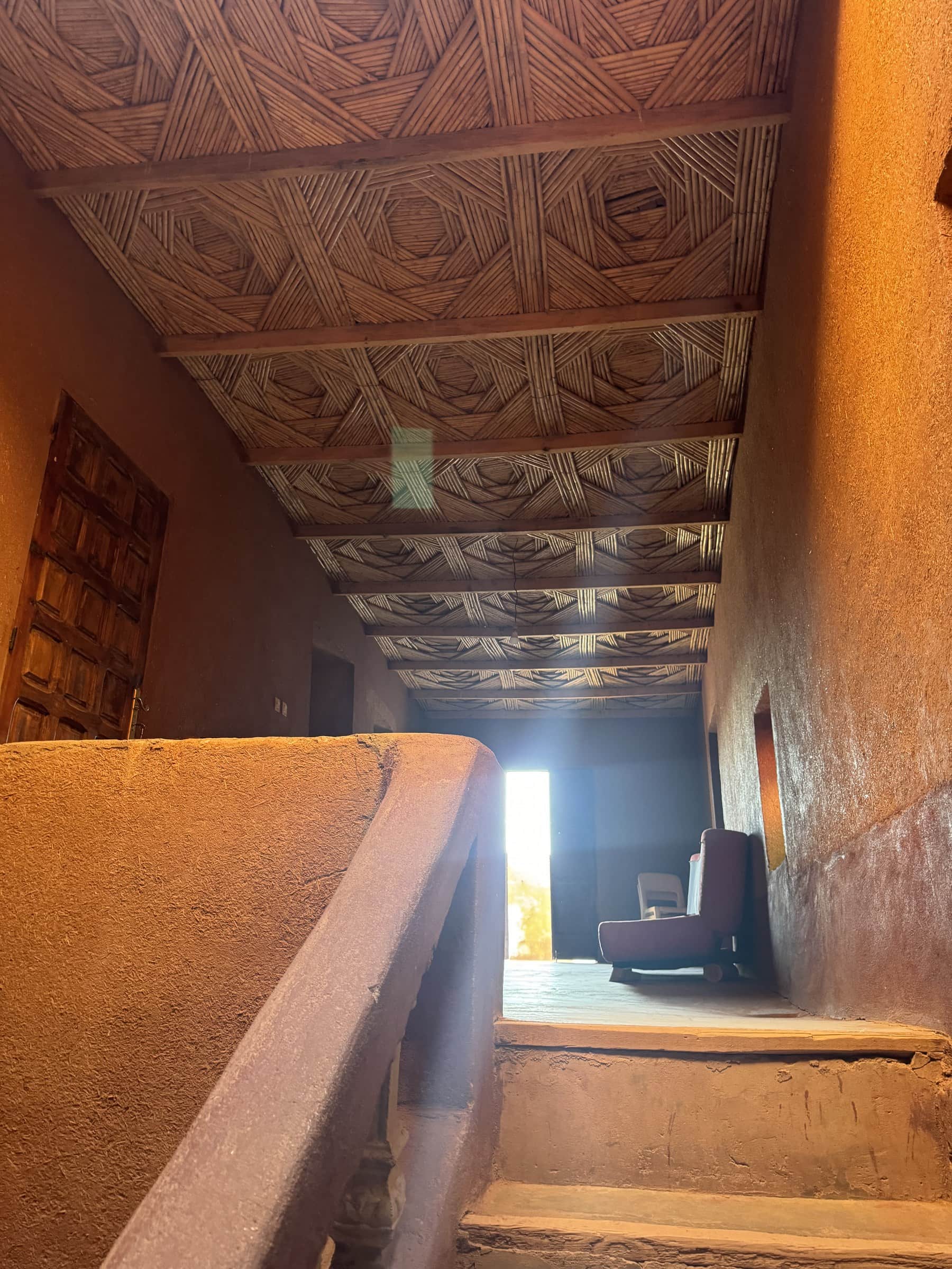 Interior de kasbah de barro con techo de cañas trenzadas y escalera de adobe en el sur de Marruecos