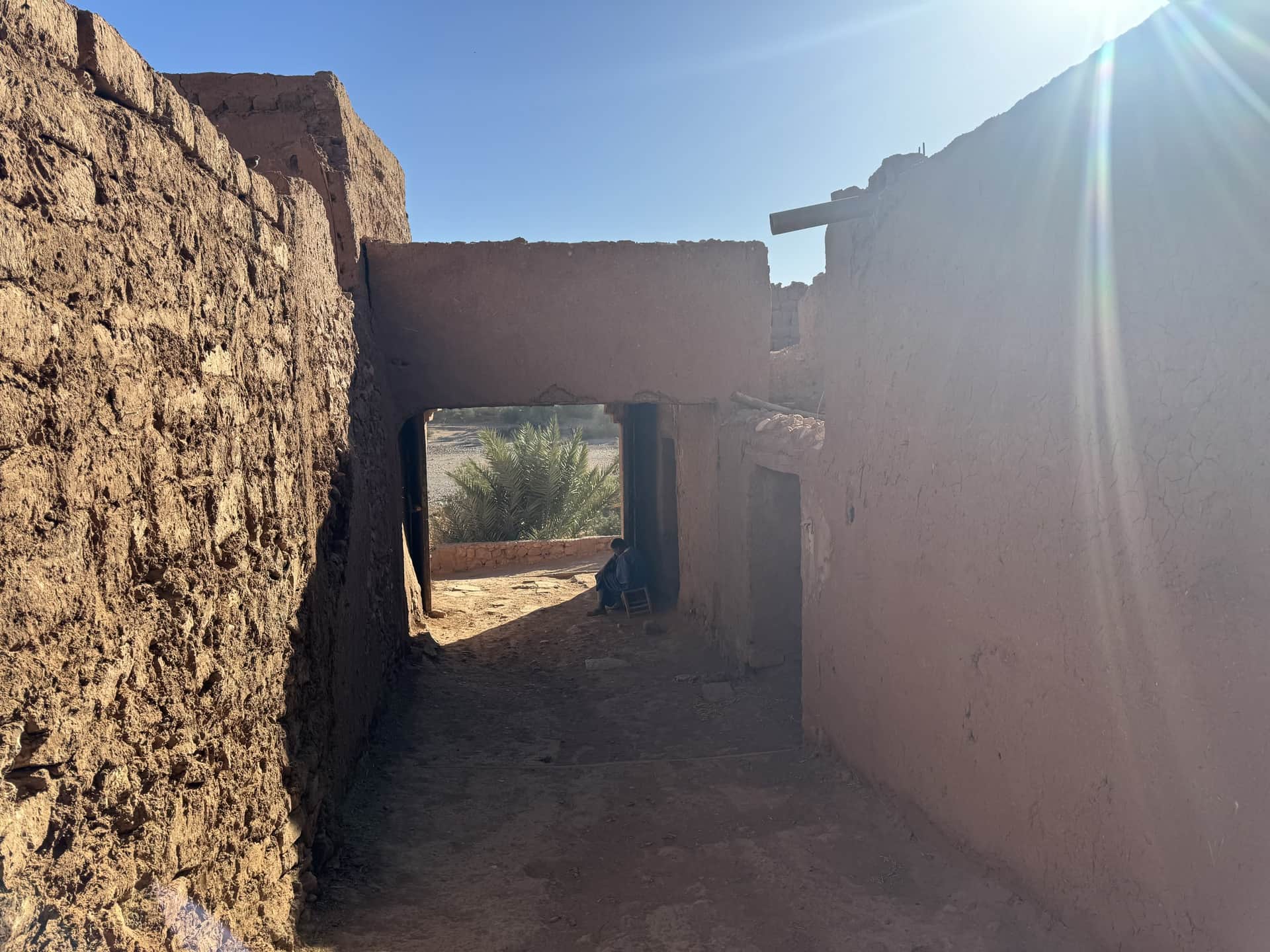 Callejón entre muros de adobe en kasbah en ruinas del sur de Marruecos con palmeras al fondo