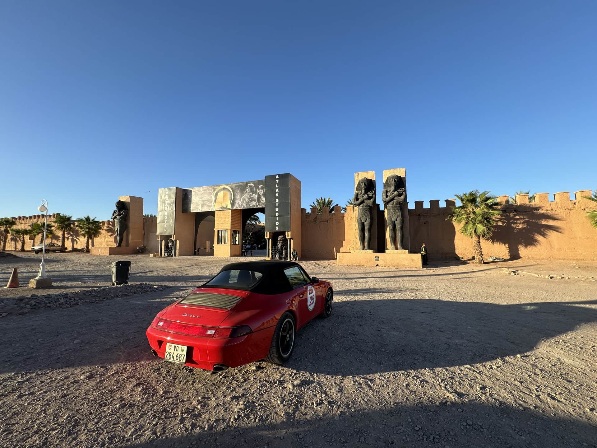 Porsche rojo descapotable frente a la entrada de Atlas Studios en Ouarzazate, Marruecos, con estatuas faraónicas