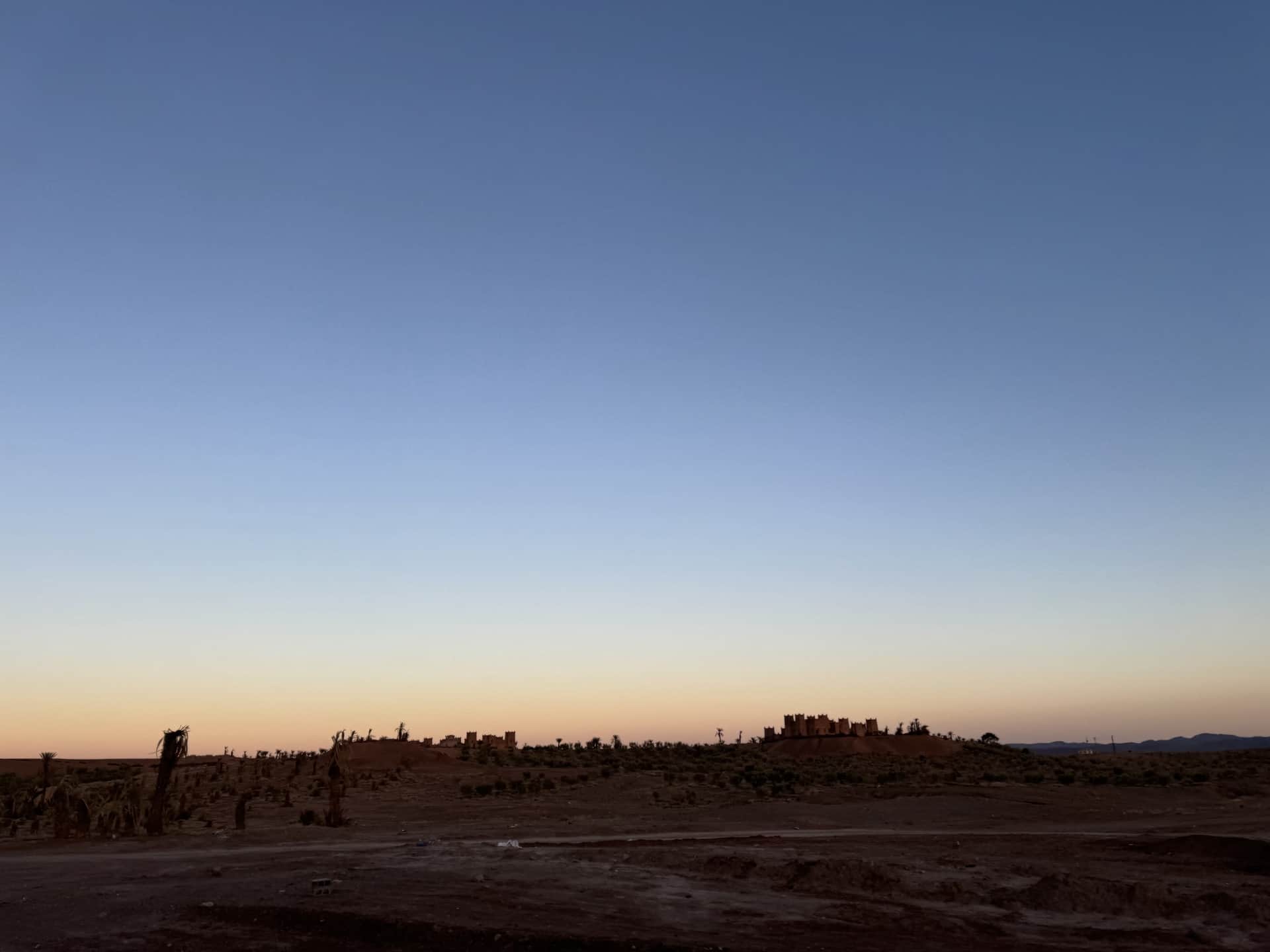 Silueta de kasbah de barro al atardecer en el sur de Marruecos con cielo degradado azul y naranja