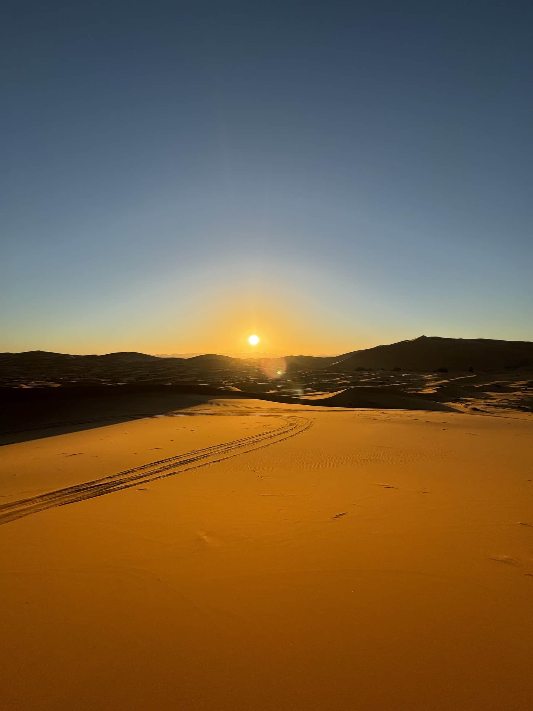 Amanecer dorado sobre las dunas de Erg Chebbi en Merzouga, con huellas de 4x4 en la arena del Sahara