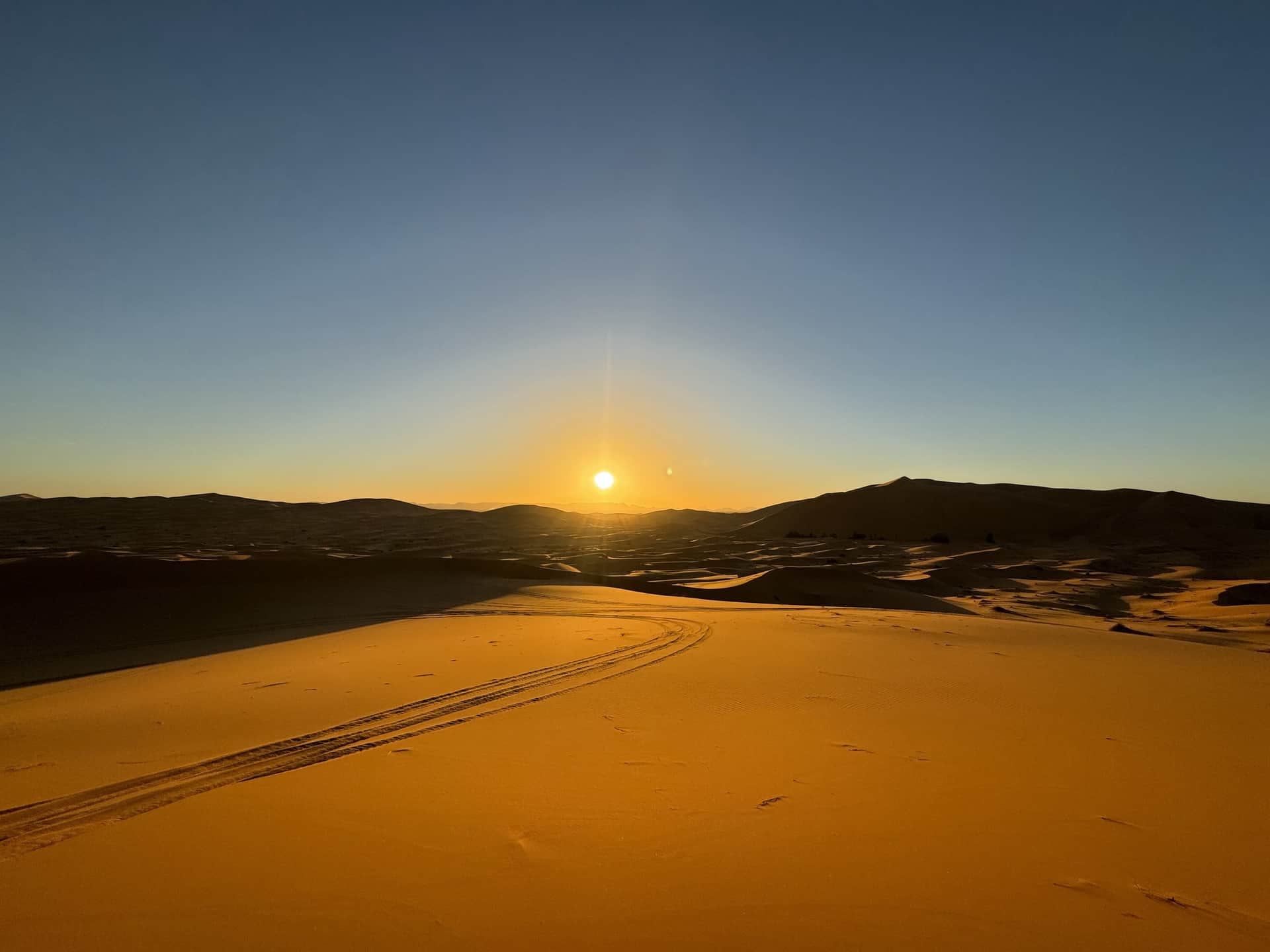 Amanecer dorado sobre las dunas del desierto de Merzouga con huellas de 4x4 en la arena del Erg Chebbi