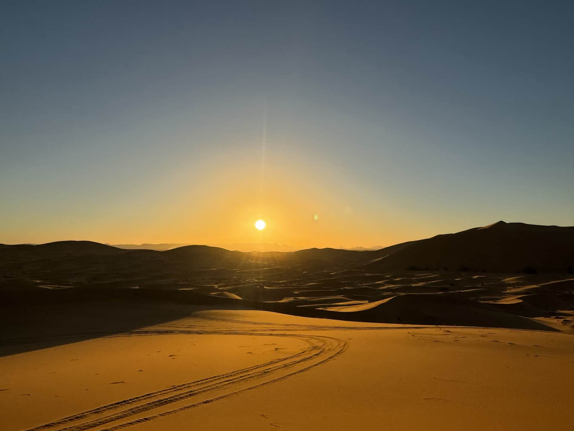 Amanecer dorado sobre las dunas del Erg Chebbi en Merzouga, con huellas de vehículo en la arena del Sahara