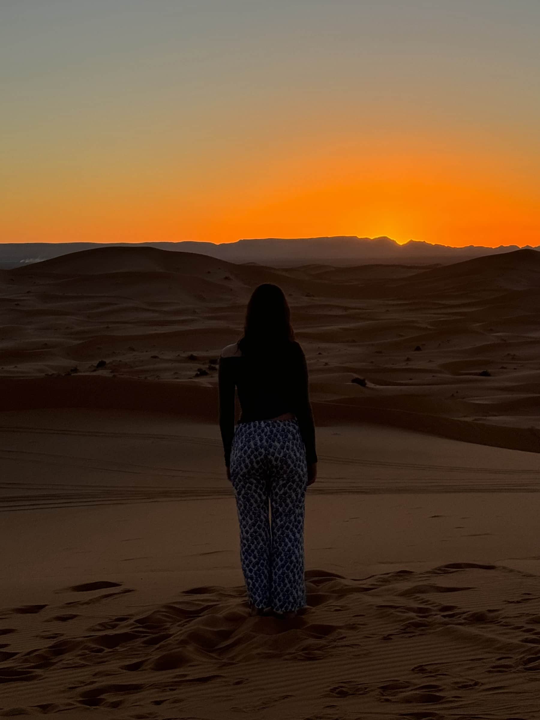 Silueta de viajera contemplando el atardecer dorado sobre las dunas del desierto de Merzouga, Sahara marroquí