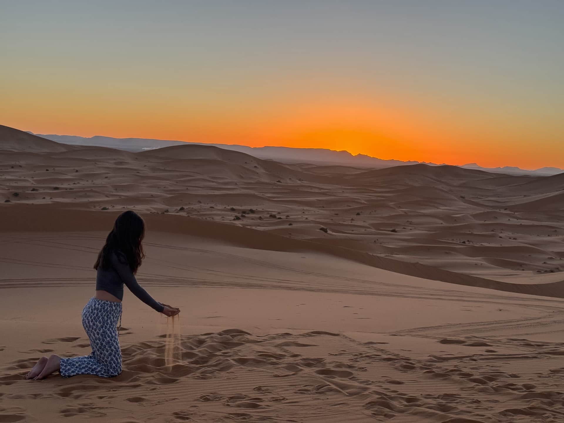 Mujer dejando caer arena entre los dedos en las dunas del Erg Chebbi al atardecer, desierto de Merzouga, Marruecos