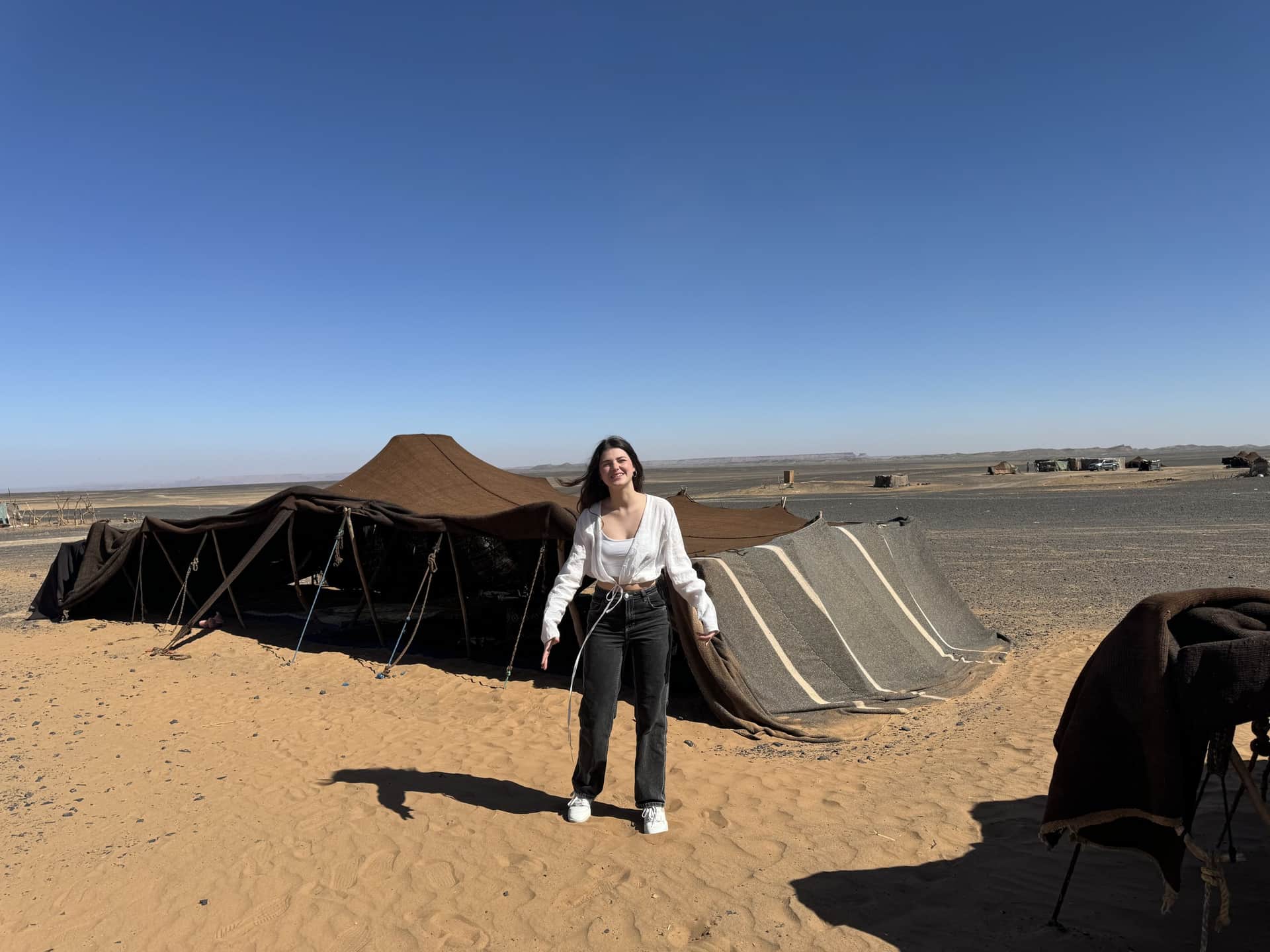 Viajera frente a jaima bereber tradicional en el desierto del Sahara de Marruecos bajo cielo azul