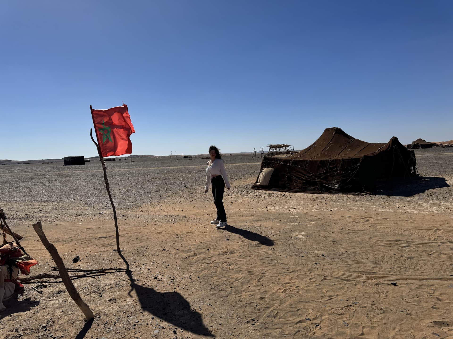 Viajera junto a tienda nómada beréber y bandera de Marruecos en el desierto del Sahara