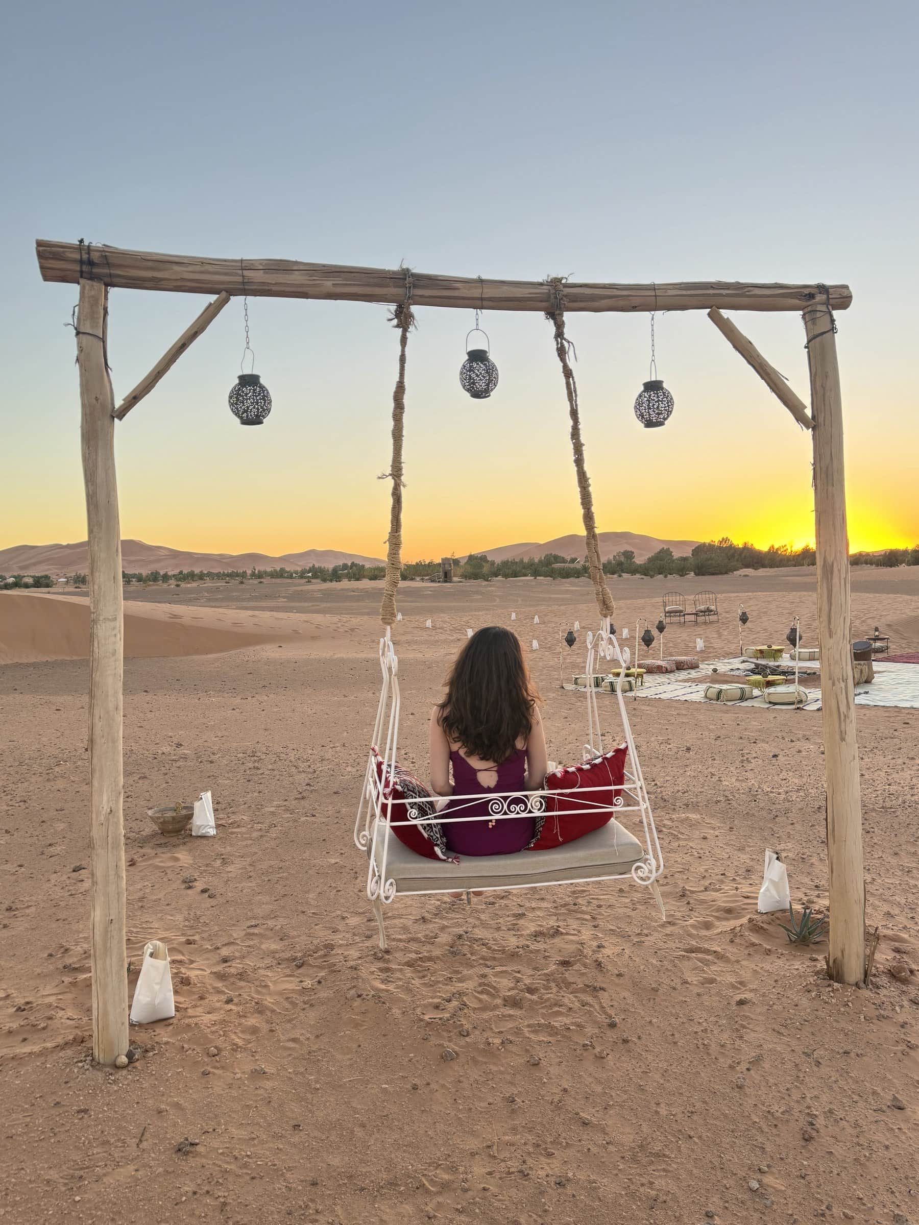 Mujer en columpio contemplando el atardecer dorado sobre las dunas del desierto de Merzouga, Sahara marroquí