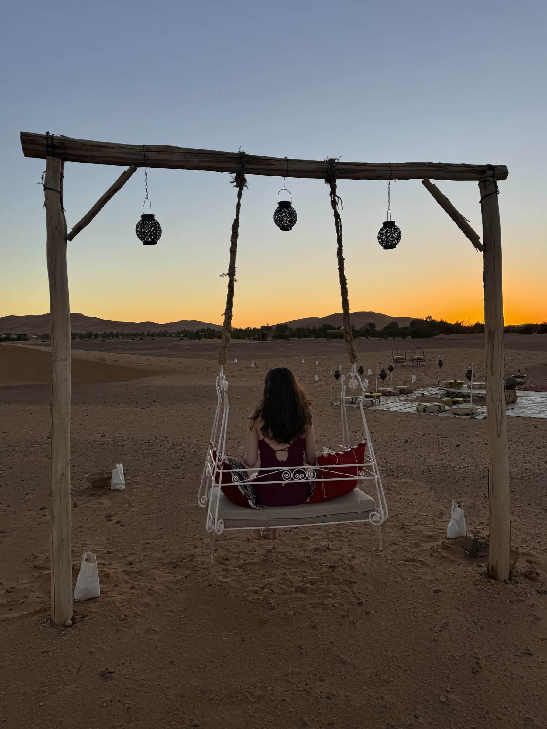 Mujer en columpio contemplando el atardecer dorado sobre las dunas del desierto de Merzouga, Marruecos