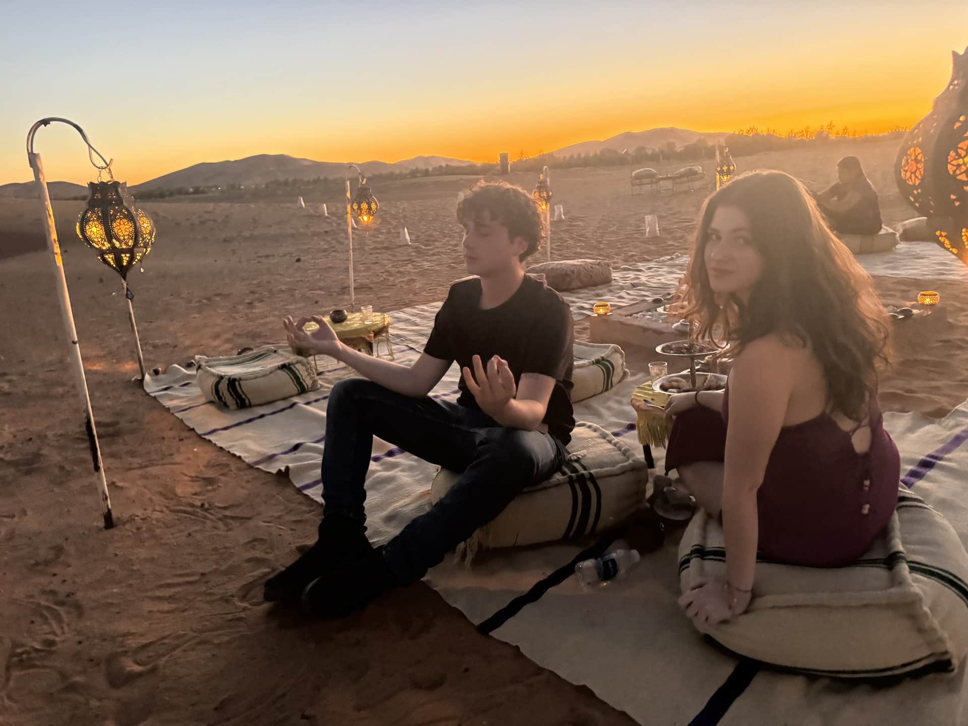 Pareja disfrutando del atardecer en el desierto de Merzouga con faroles marroquíes y cojines sobre la arena