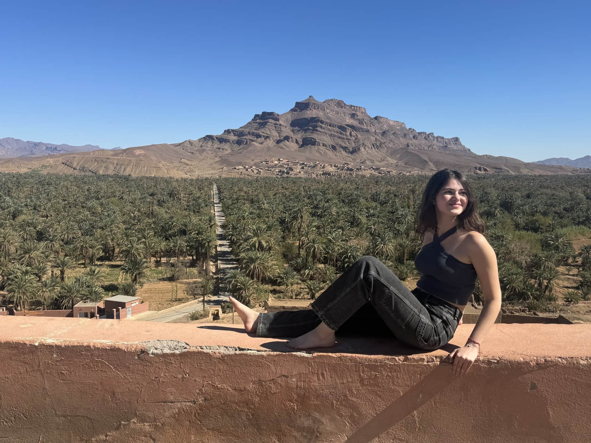 Viajera sentada en terraza con vistas al palmeral del Valle del Draa y montañas rocosas en Marruecos