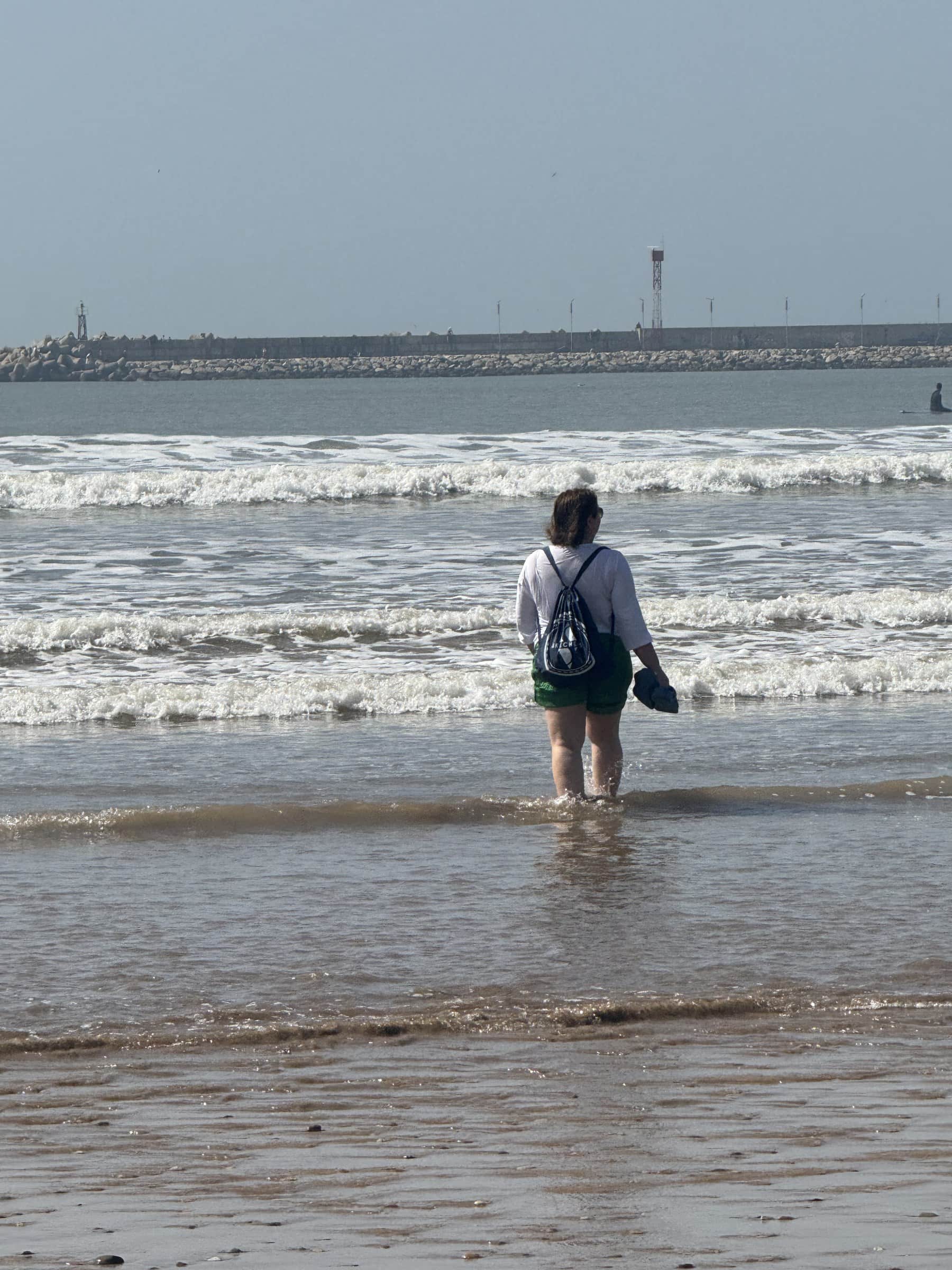Viajera caminando por la orilla del mar en una playa atlántica de Marruecos con rompeolas al fondo