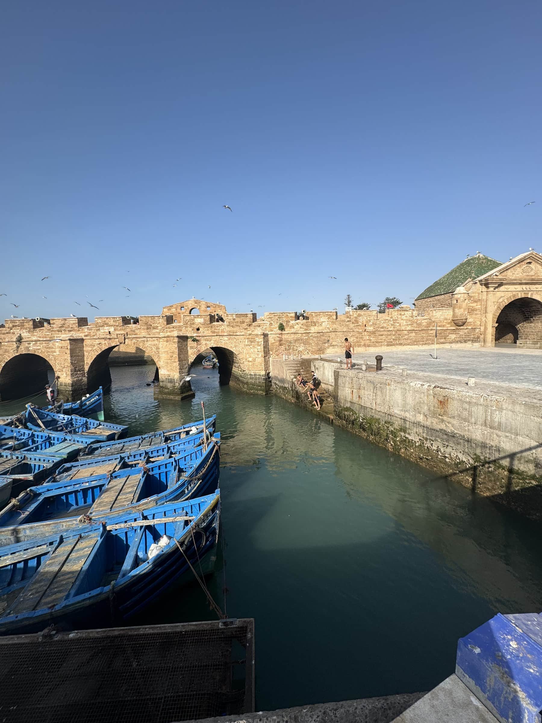 Puerto pesquero de Essaouira con barcas azules tradicionales y murallas históricas al fondo, Marruecos
