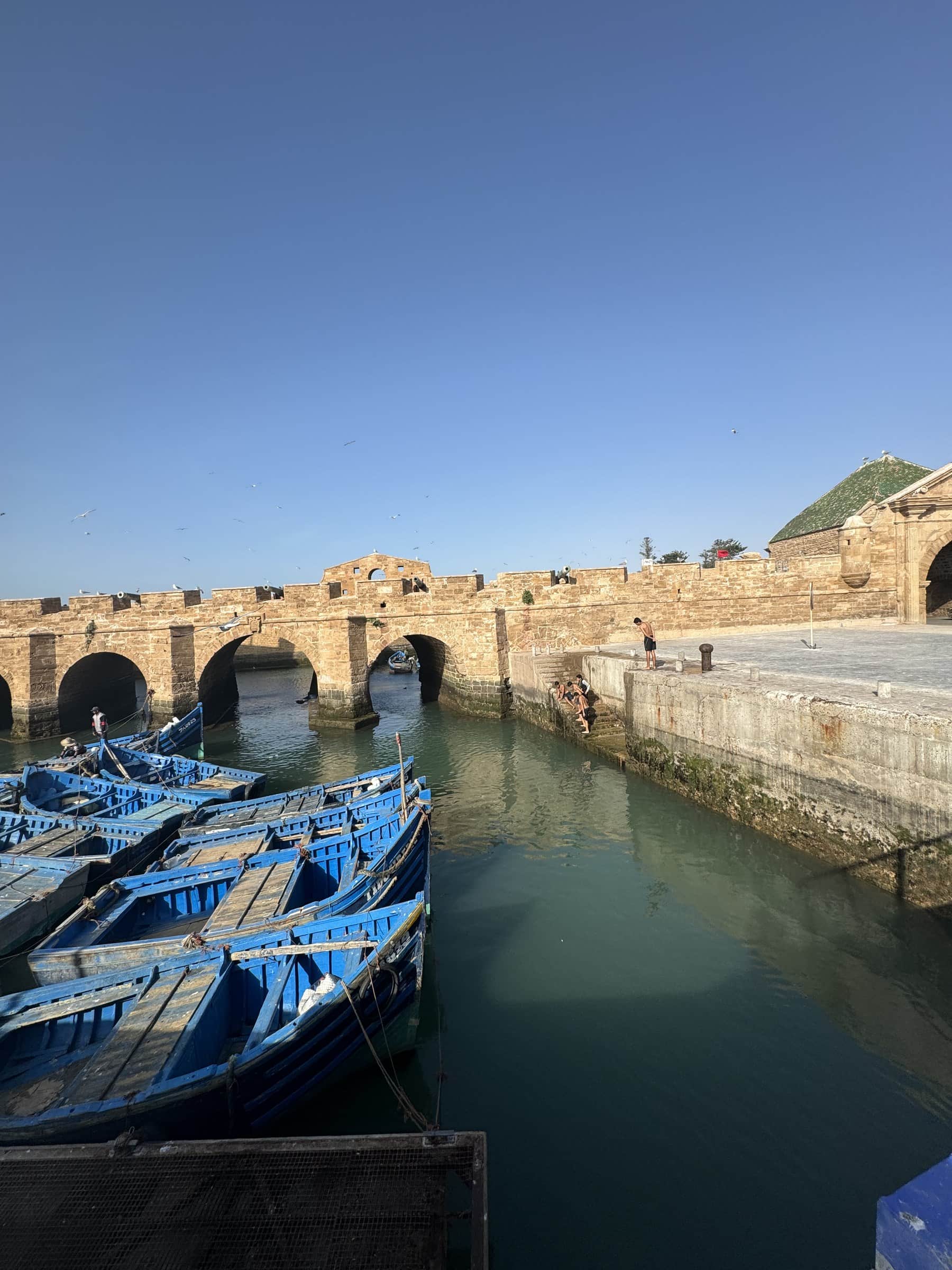 Puerto pesquero de Essaouira con barcas azules tradicionales y murallas históricas de piedra al fondo, Marruecos
