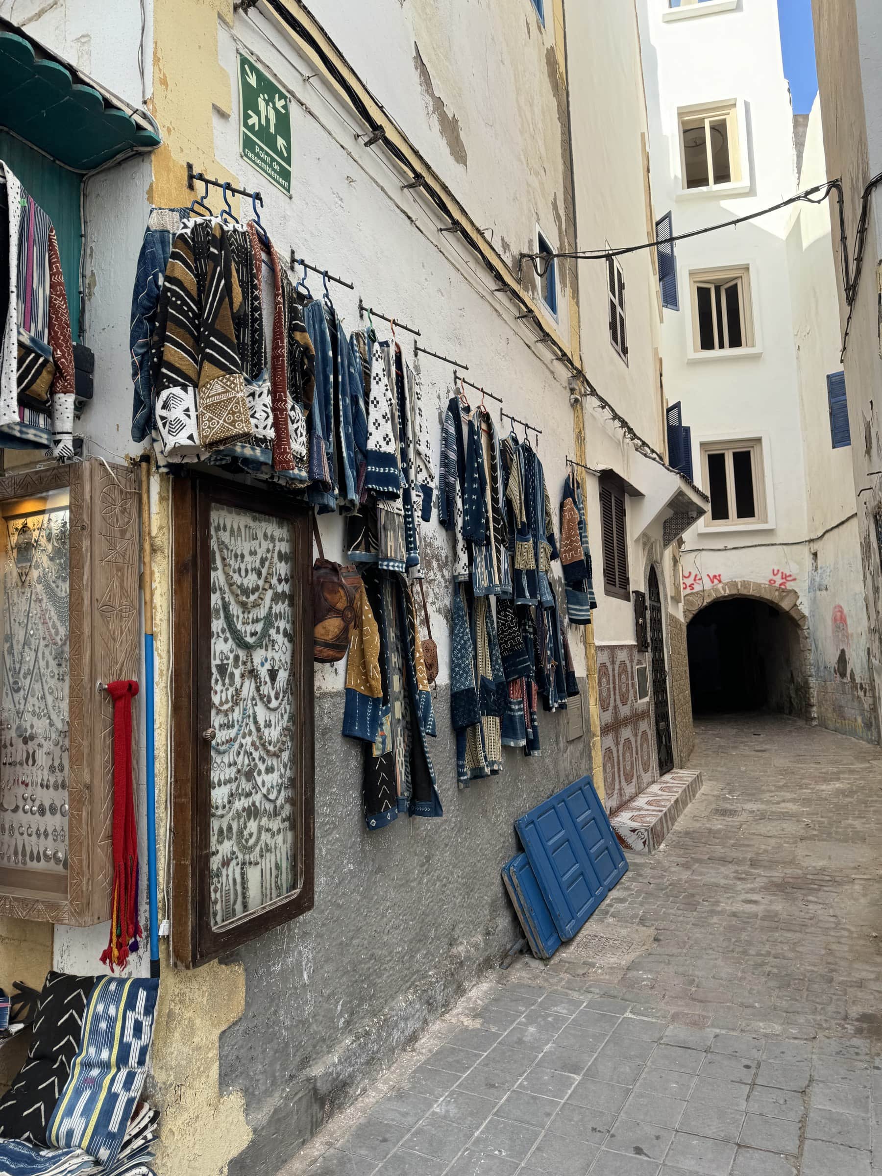 Callejón de la medina de Tánger con ropa artesanal y textiles bereberes colgados en la fachada de una tienda