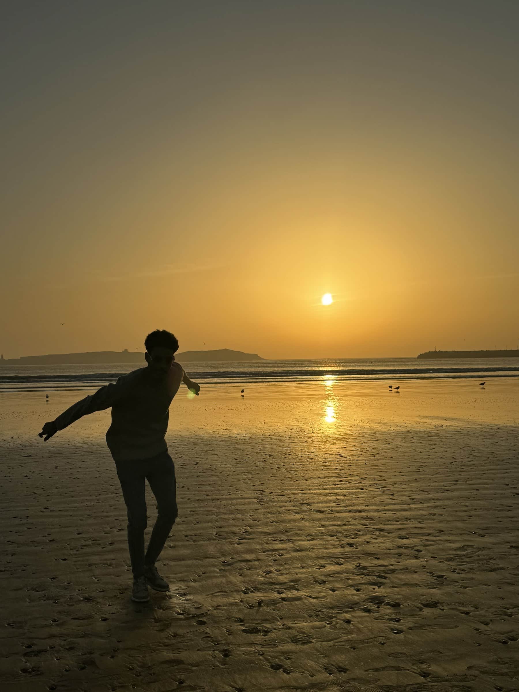 Silueta de persona bailando en la playa de Essaouira al atardecer con el sol dorado sobre el Atlántico