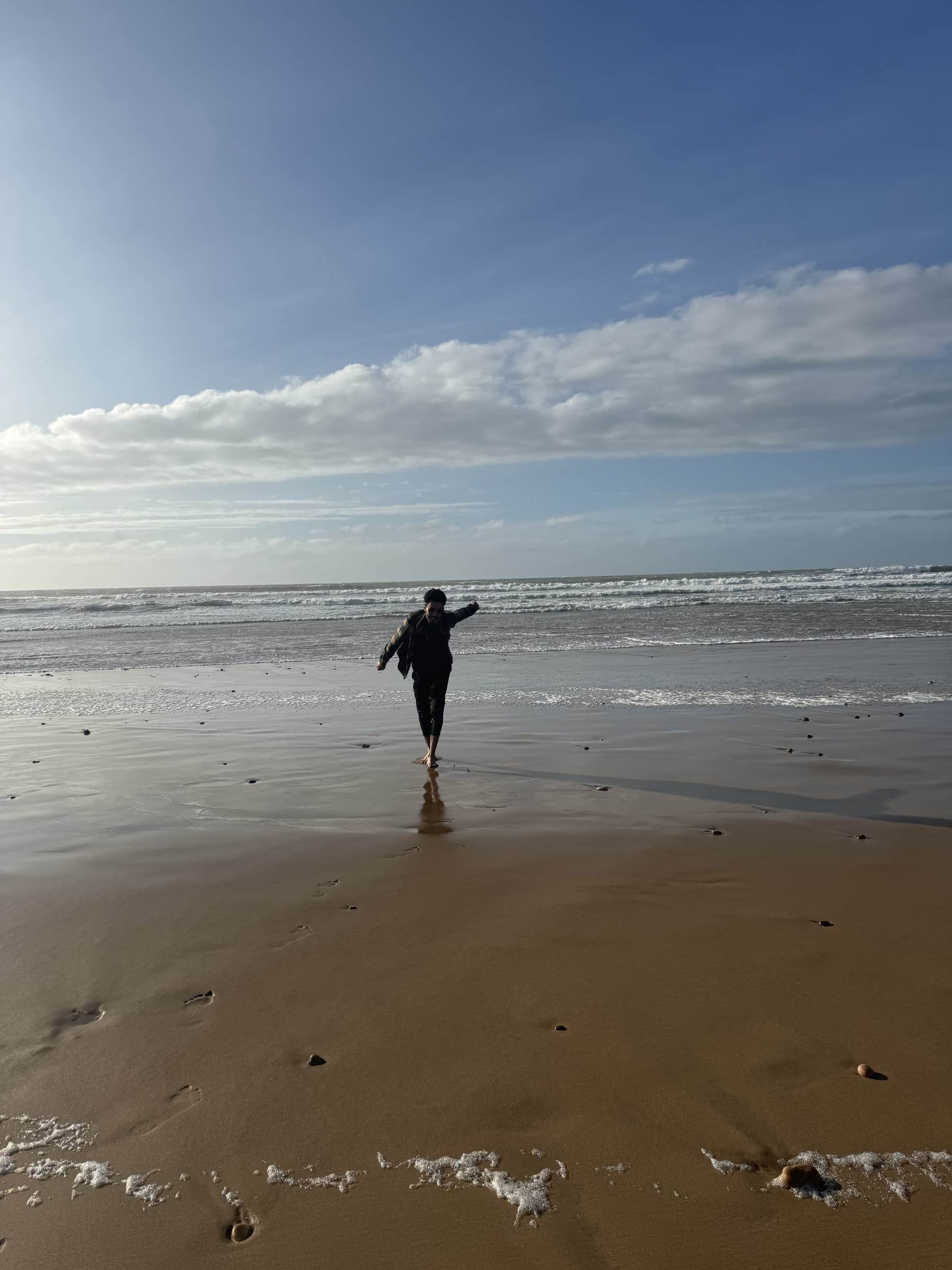 Persona caminando descalza por la playa atlántica de Marruecos con olas y cielo azul al fondo