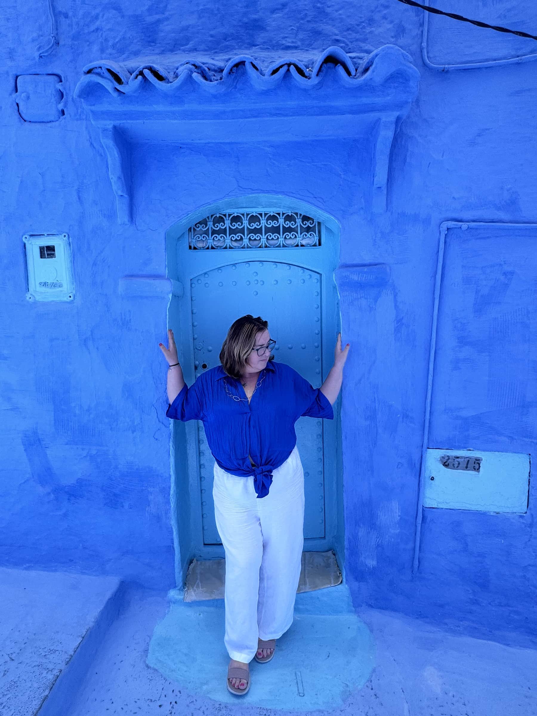 Viajera posando ante una puerta azul con forja en la medina de Chefchaouen, Marruecos