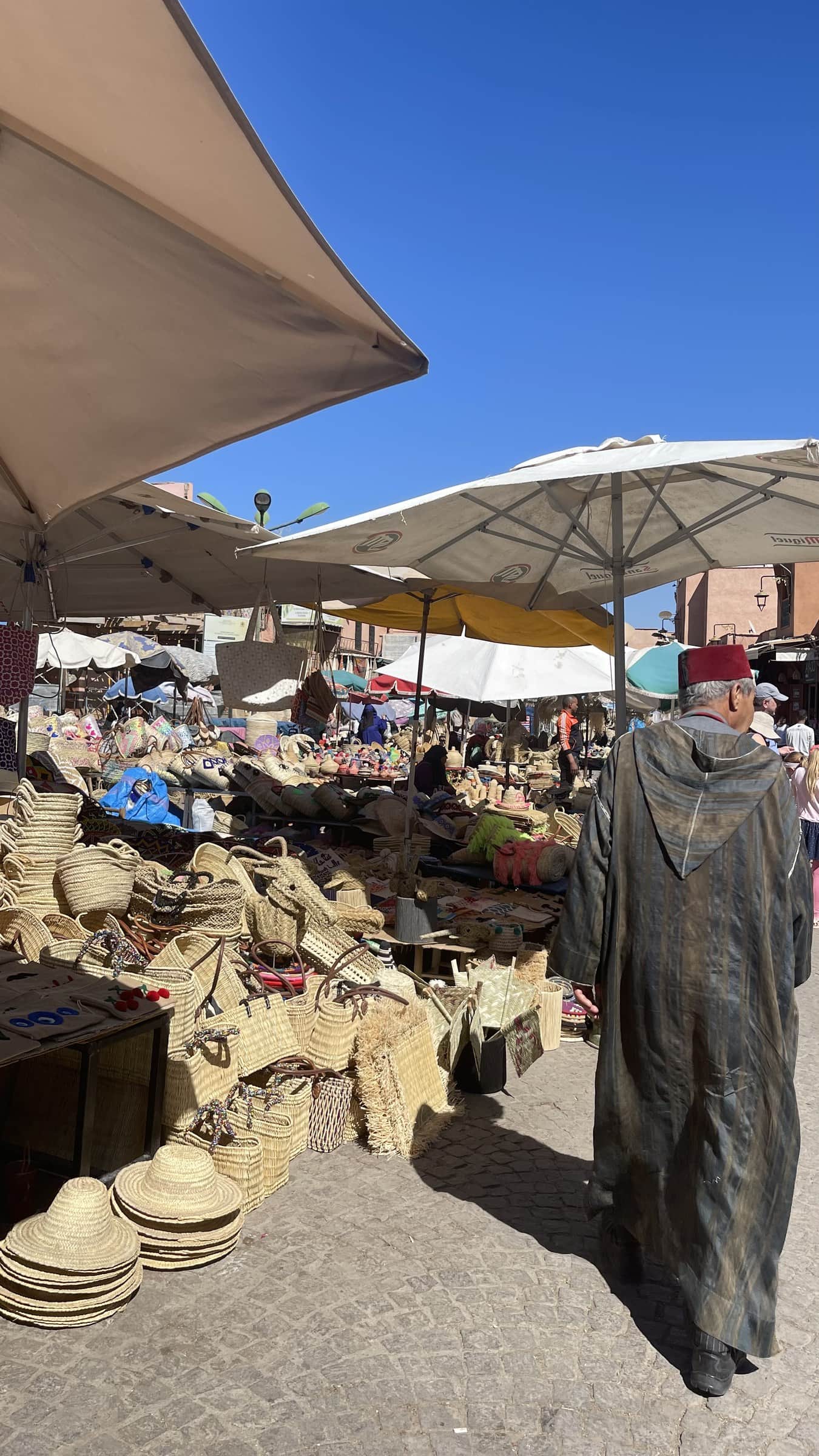 Mercado al aire libre en Marrakech con cestas de esparto y hombre en djellaba y fez rojo entre puestos de artesanía