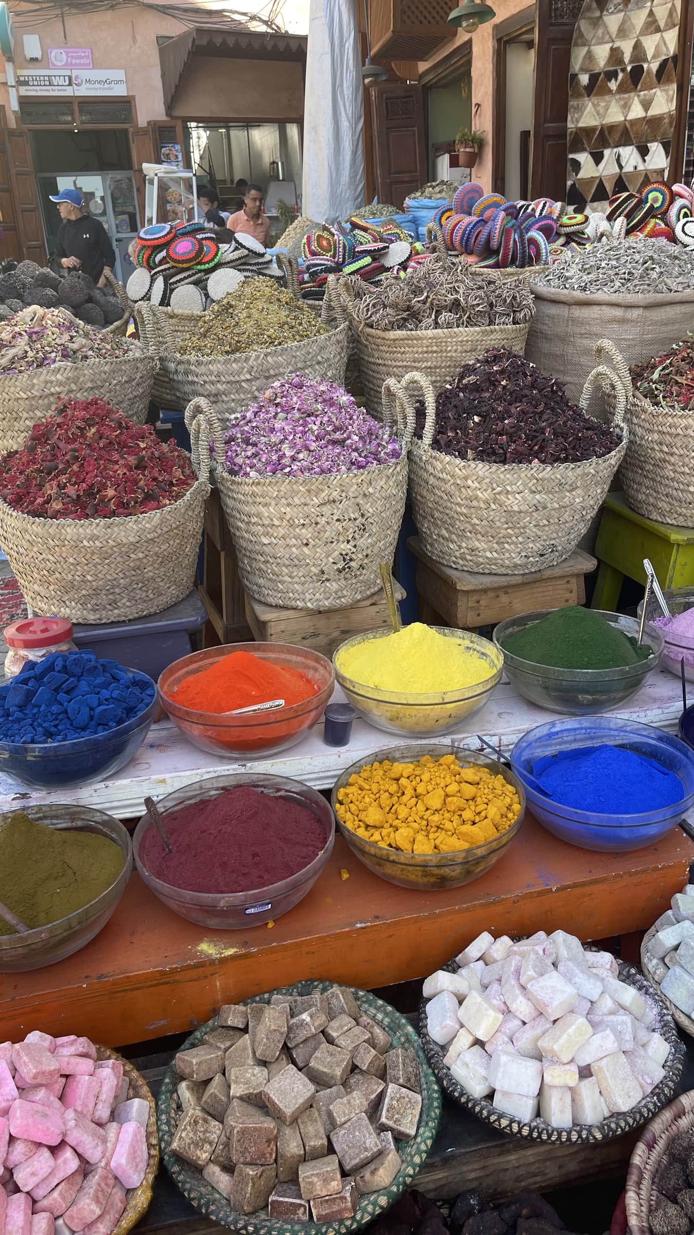 Puesto de especias y hierbas en el zoco de Marrakech con coloridos polvos y flores secas en cestas