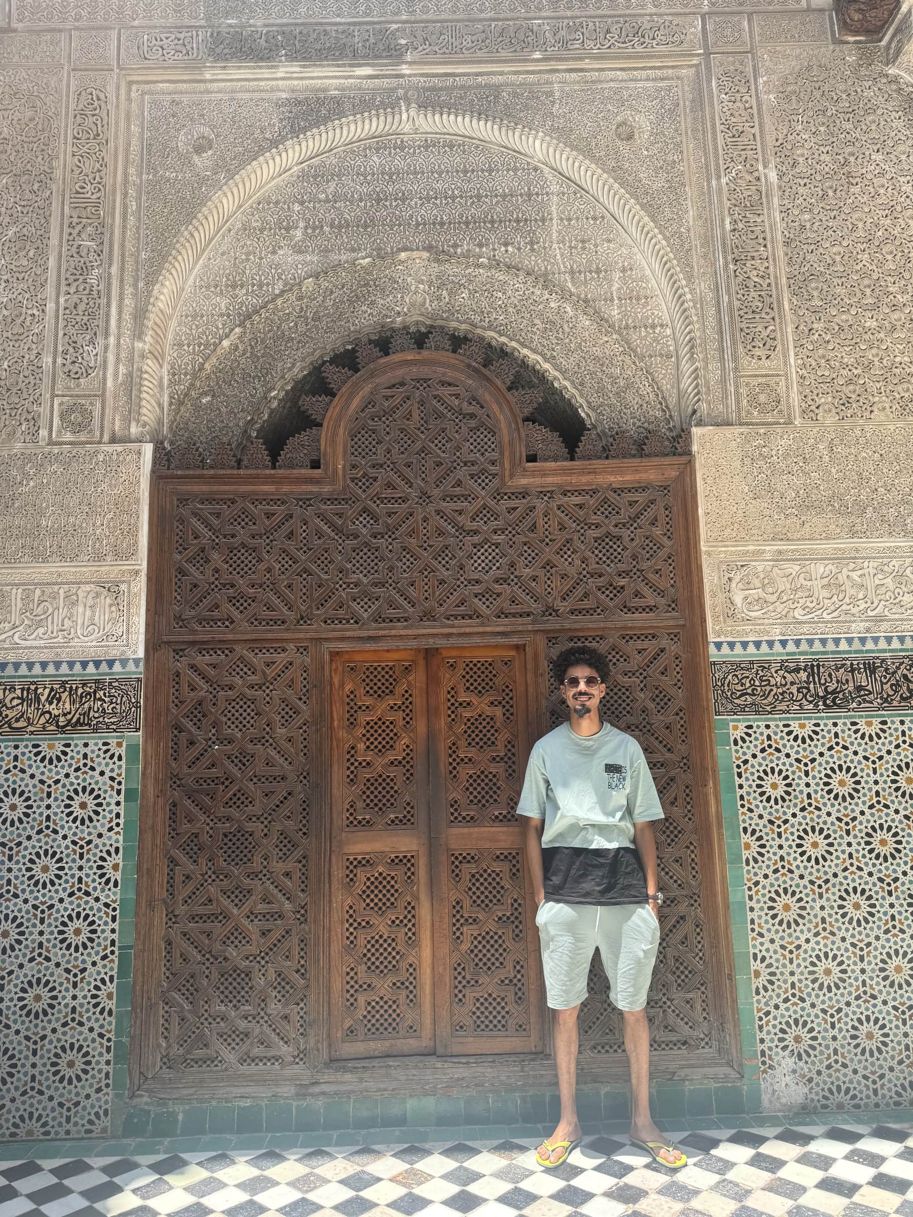 Turista posando ante puerta de madera tallada con arco de yeso y mosaicos en la medina de Fez, Marruecos