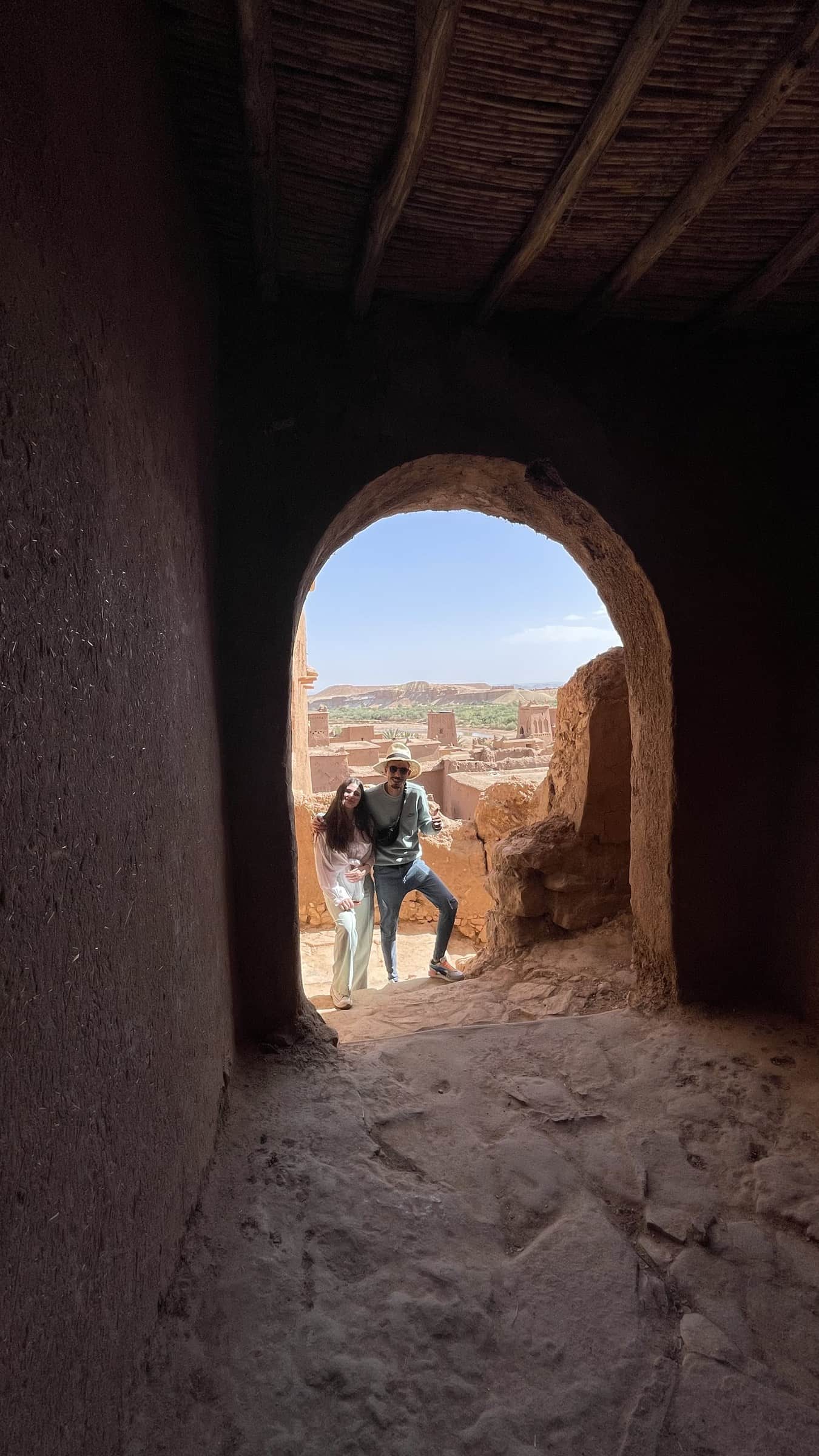 Pareja de viajeros posando en arco de barro de Aït Ben Haddou con vistas a la kasbah UNESCO y oasis, Marruecos