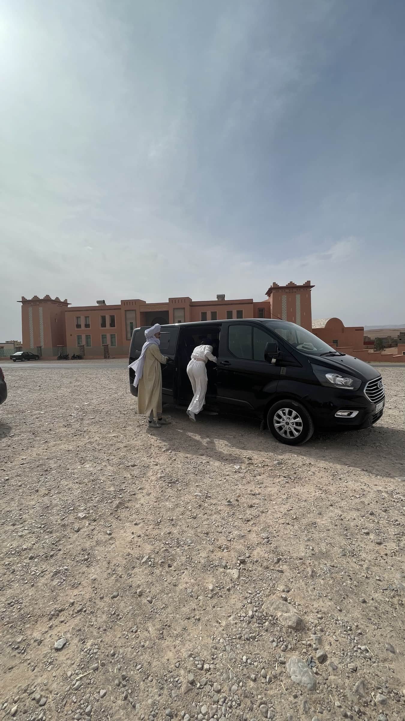 Guías bereberes con túnica blanca subiendo a furgoneta privada negra en el desierto de Merzouga, Marruecos
