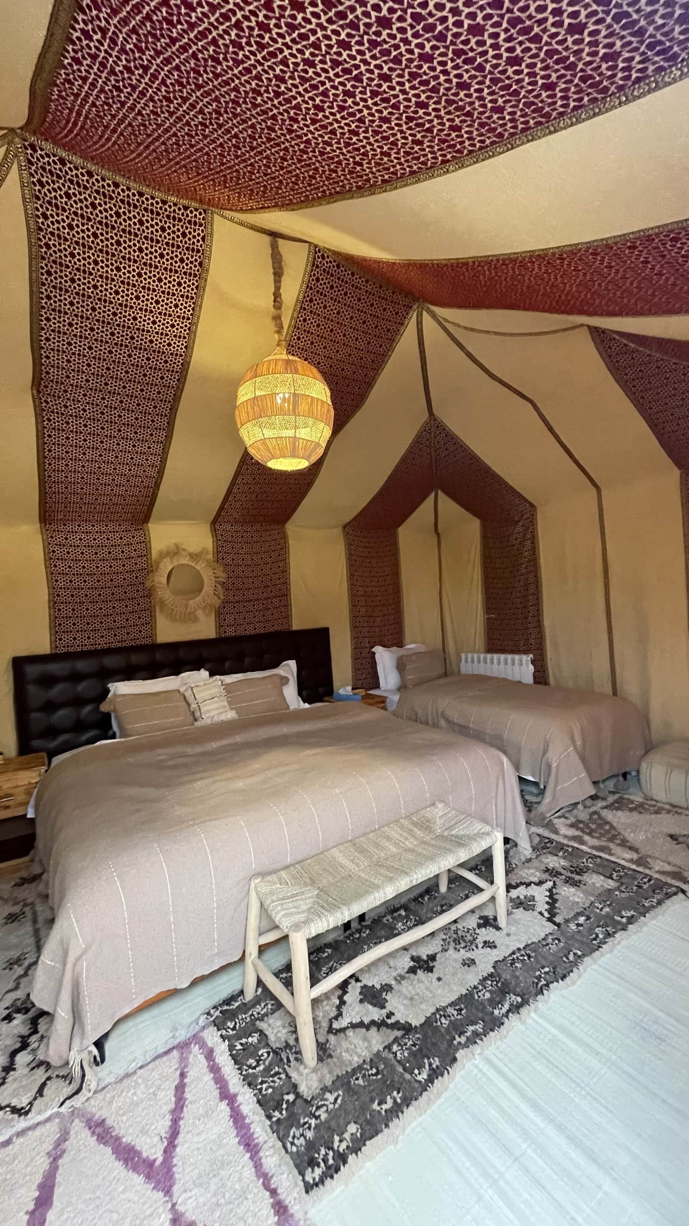 Interior de jaima de lujo en el desierto de Merzouga con dos camas, alfombras bereberes y lámpara artesanal