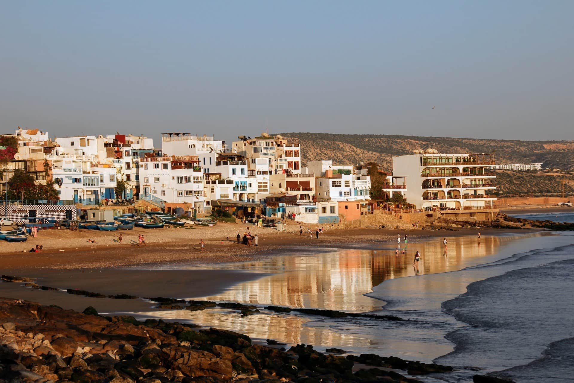 Playa de Taghazout al atardecer con casas blancas y azules reflejadas en el agua, costa atlántica de Marruecos