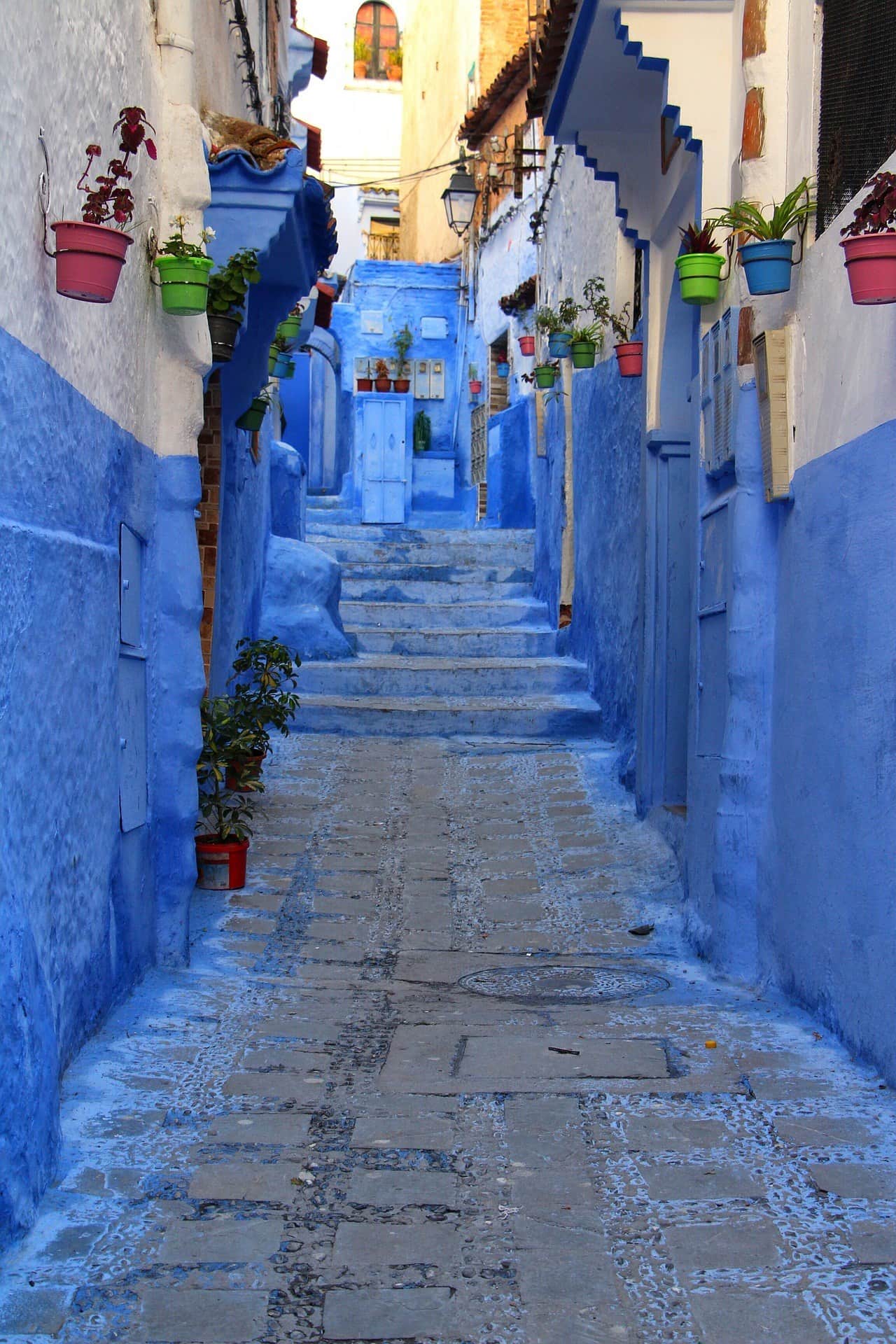 Callejón azul con escaleras y macetas de colores en la medina de Chefchaouen, la ciudad azul de Marruecos