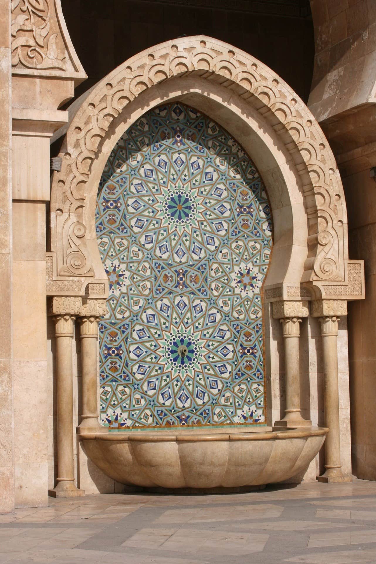Fuente de mármol con mosaico de zellige azul y verde en la Mezquita Hassan II de Casablanca, Marruecos