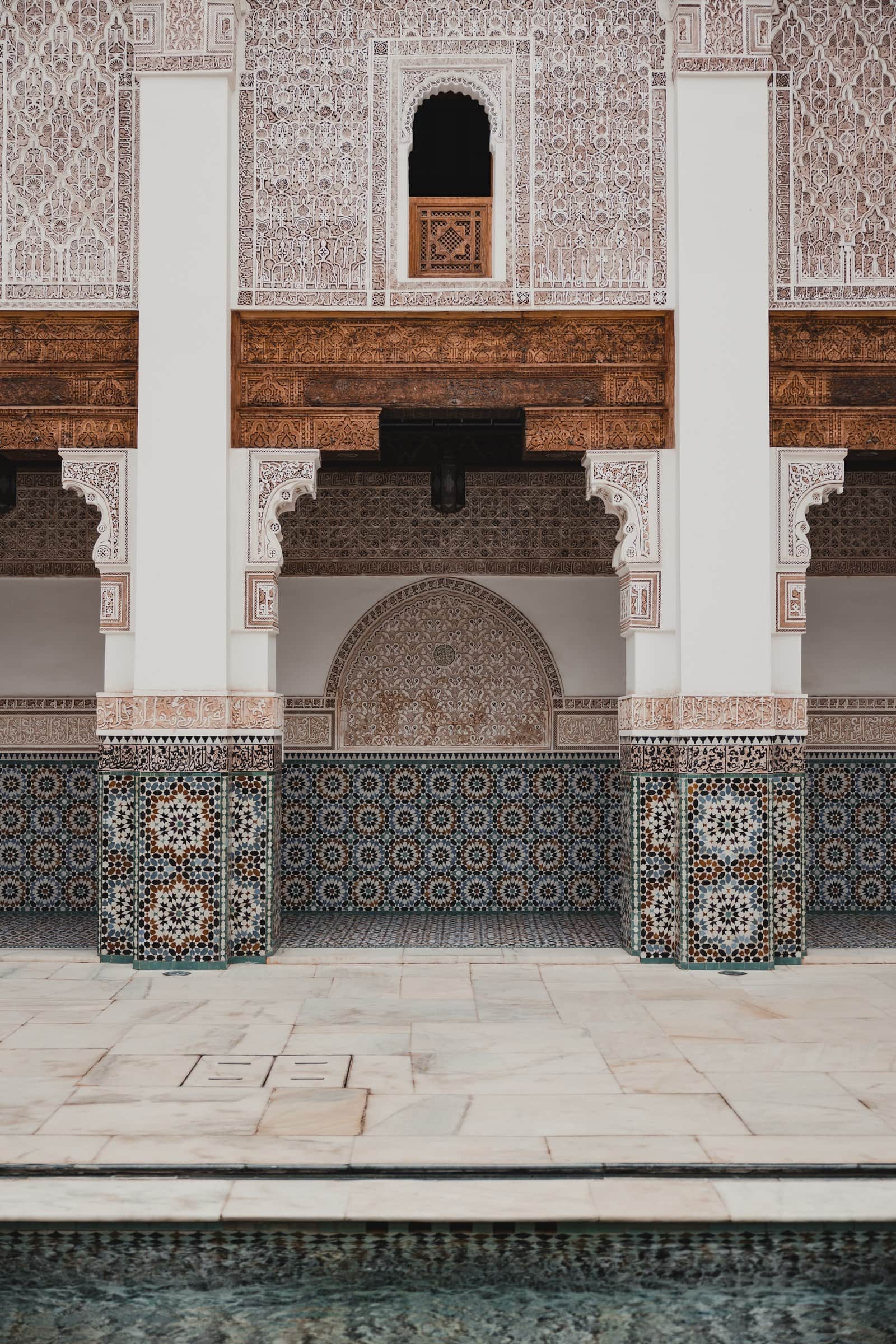 Patio interior de madrasa marroquí con zócalo de mosaicos zellige, arcos de yeso tallado y estanque reflectante
