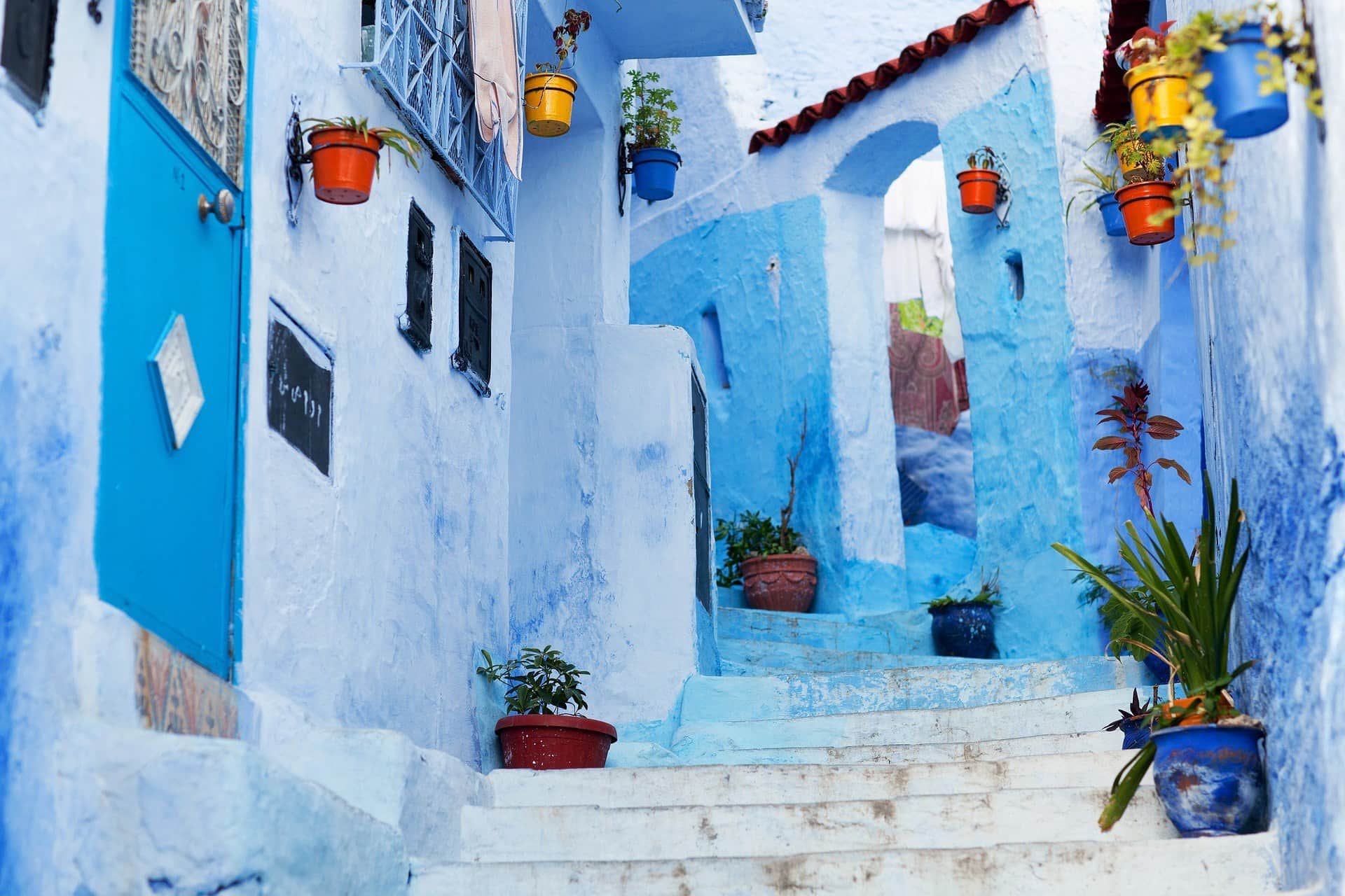 Callejón azul de Chefchaouen con escaleras blancas y macetas de colores en las paredes de la medina