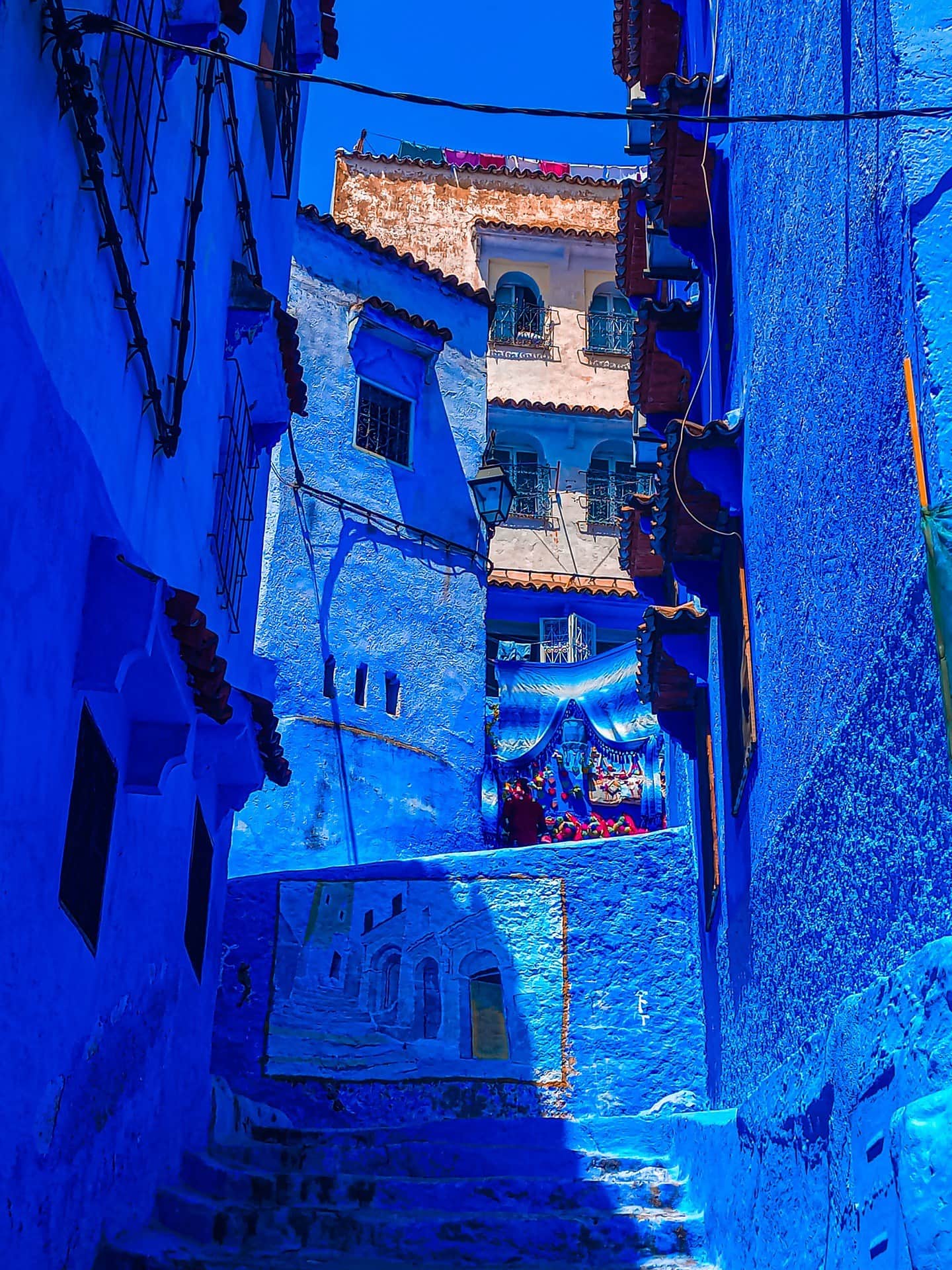 Callejón azul de Chefchaouen con escaleras, ropa tendida y puesto artesanal entre edificios pintados de azul