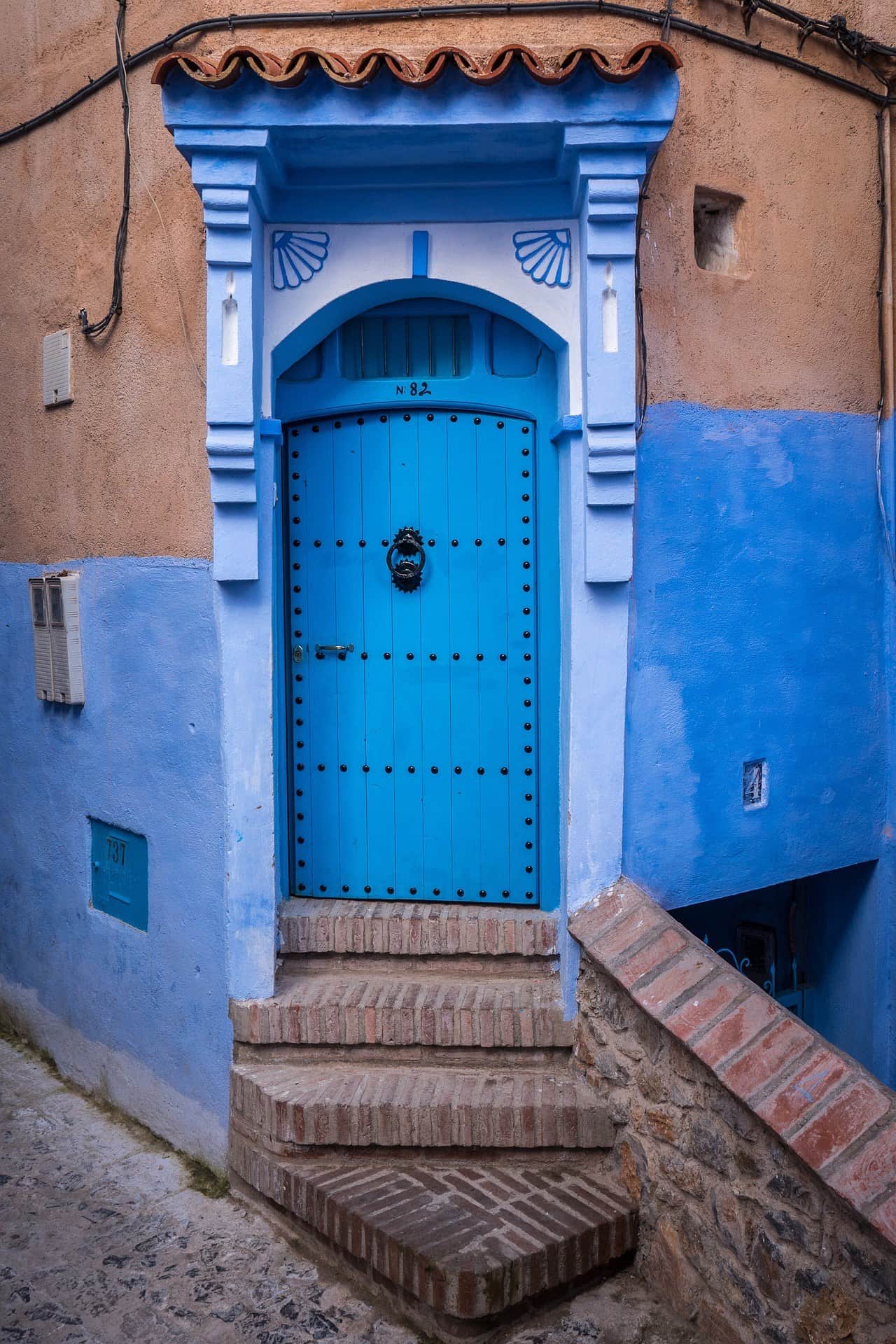 Puerta azul tradicional con aldaba de hierro y escalones de ladrillo en la medina de Chefchaouen, Marruecos
