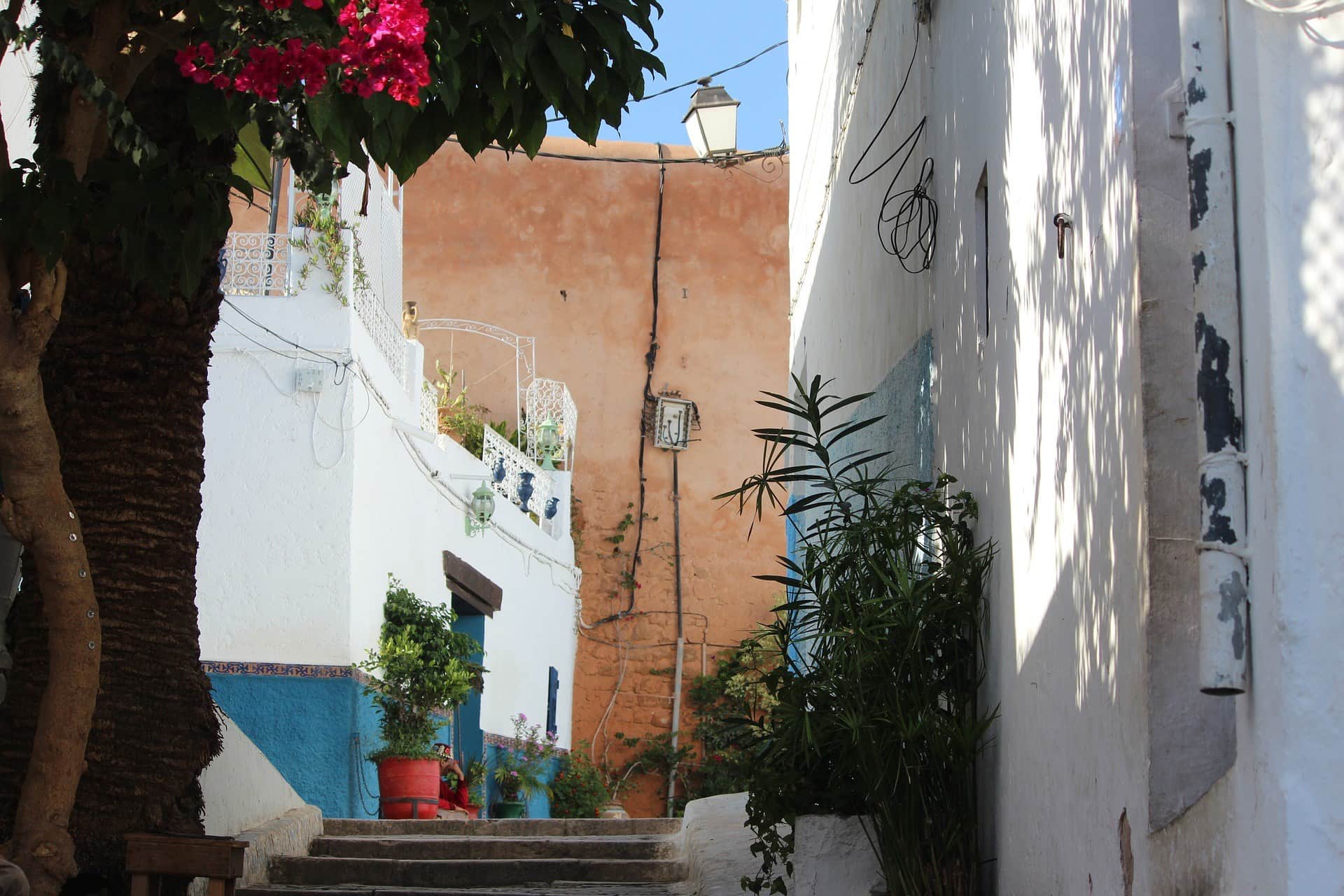 Callejón de la medina de Rabat con casas blancas y azules, buganvilla rosa y escaleras de piedra