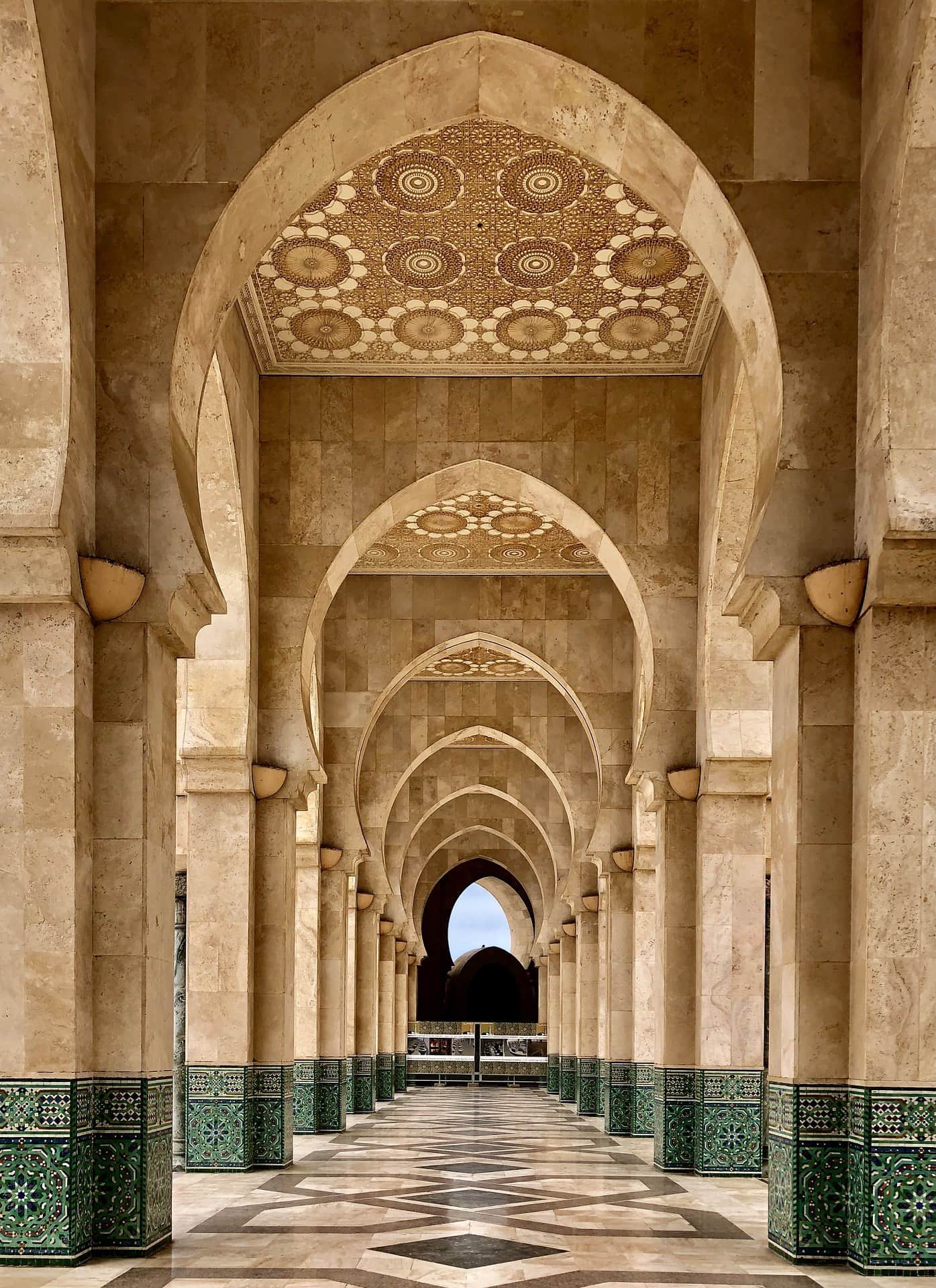 Galería de arcos de la Mezquita Hassan II en Casablanca con techos de mosaicos dorados y zócalos de azulejos verdes