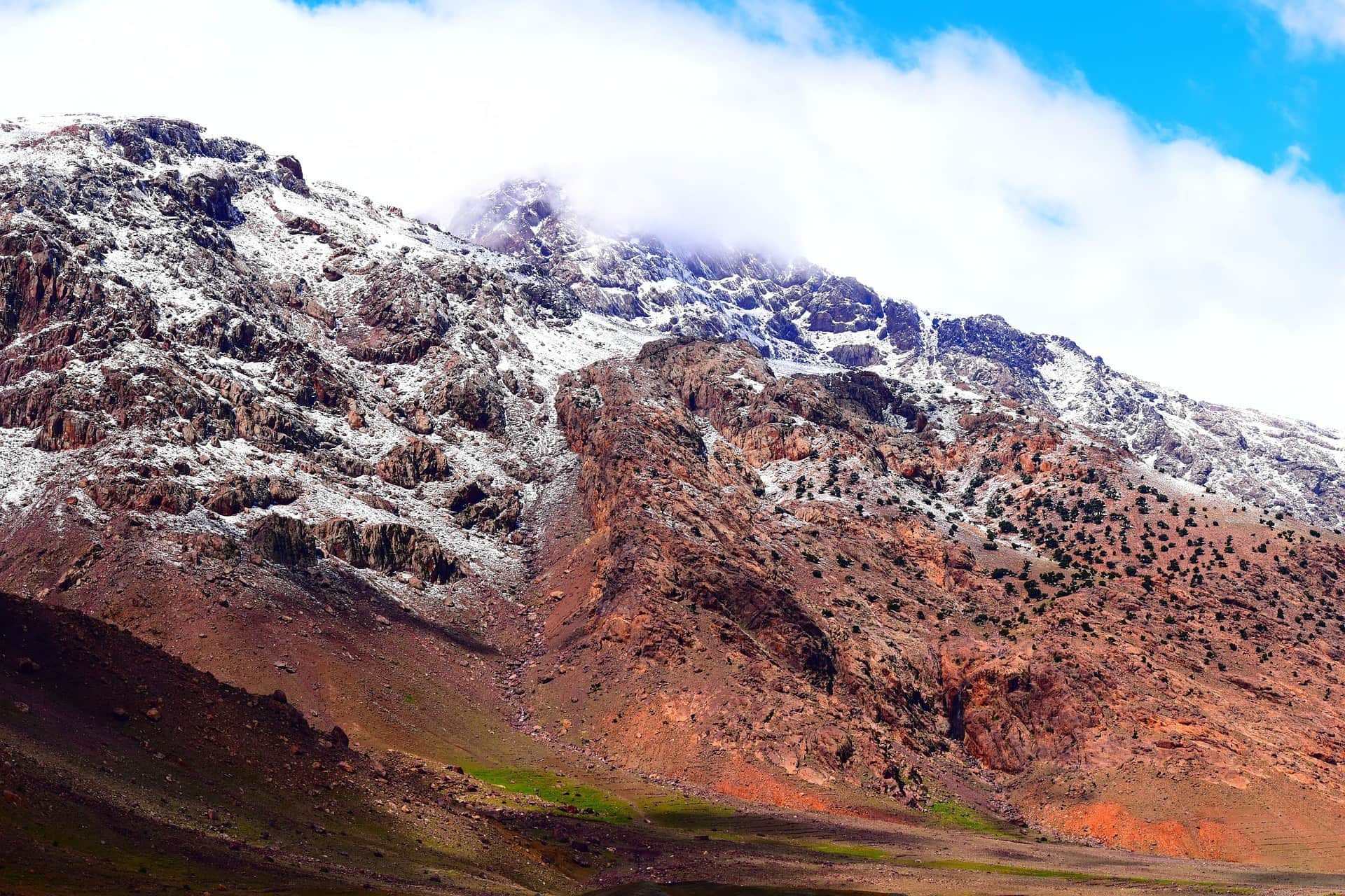Cumbres nevadas del Alto Atlas marroquí con rocas rojizas y cielo azul en invierno
