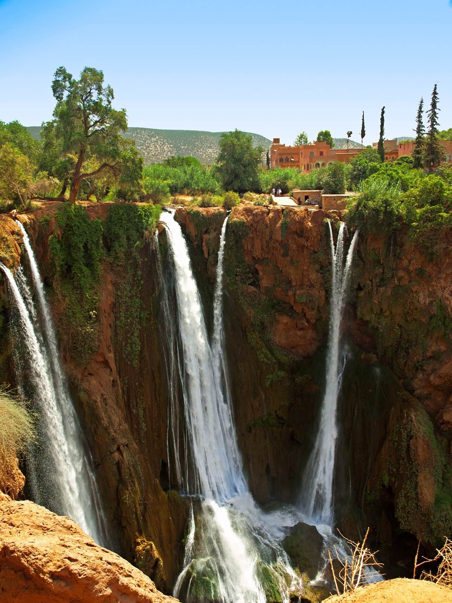 Cascadas de Ouzoud cayendo sobre acantilados rojizos rodeados de vegetación verde en Marruecos
