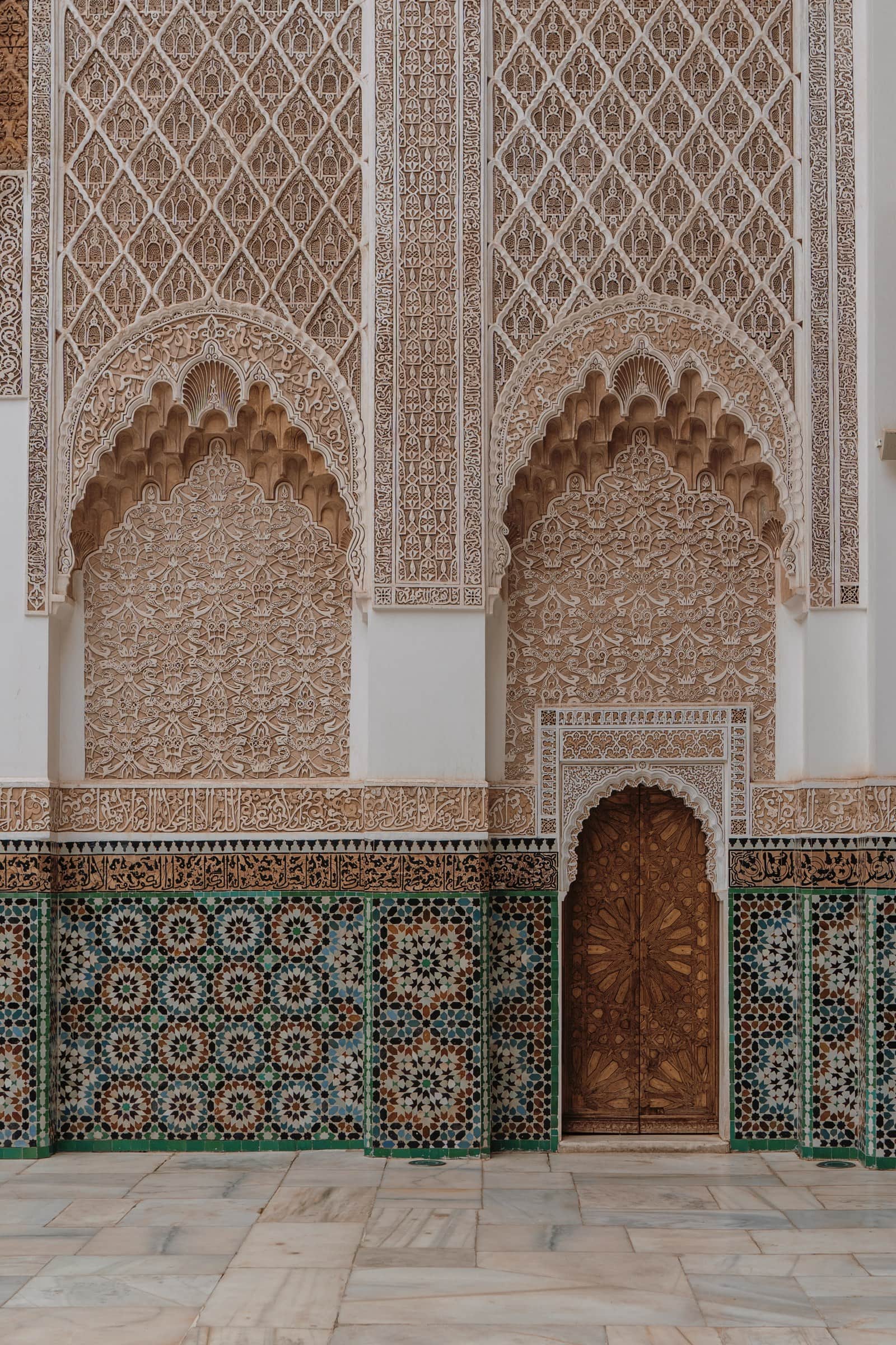 Intrincados arabescos y zócalo de azulejos en madrasa marroquí con puerta de madera tallada