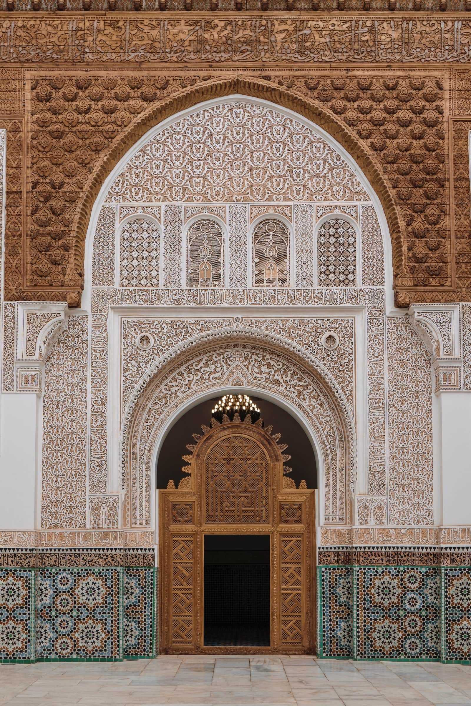 Madrasa Ben Youssef de Marrakech: arco de yesería tallada, puerta dorada y zócalo de mosaico tradicional marroquí