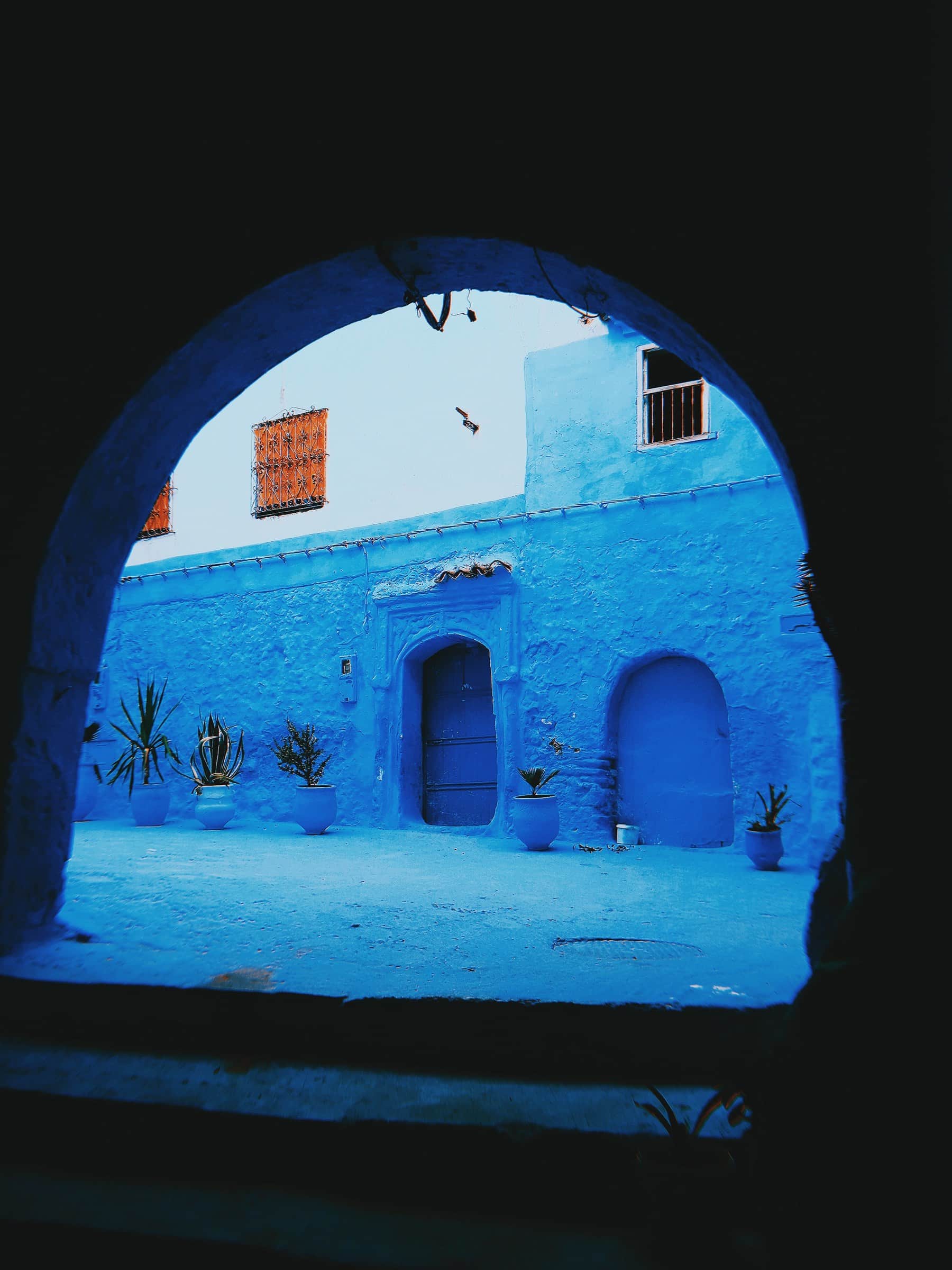 Arco de piedra enmarcando patio de casas pintadas de azul intenso con puertas y macetas en Chefchaouen, Marruecos